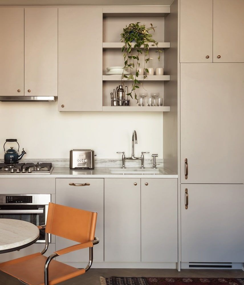 Warm beige cabinetry and copper hardware create an inviting kitchen corner, where trailing plants soften minimalist lines and natural light illuminates thoughtful design details.