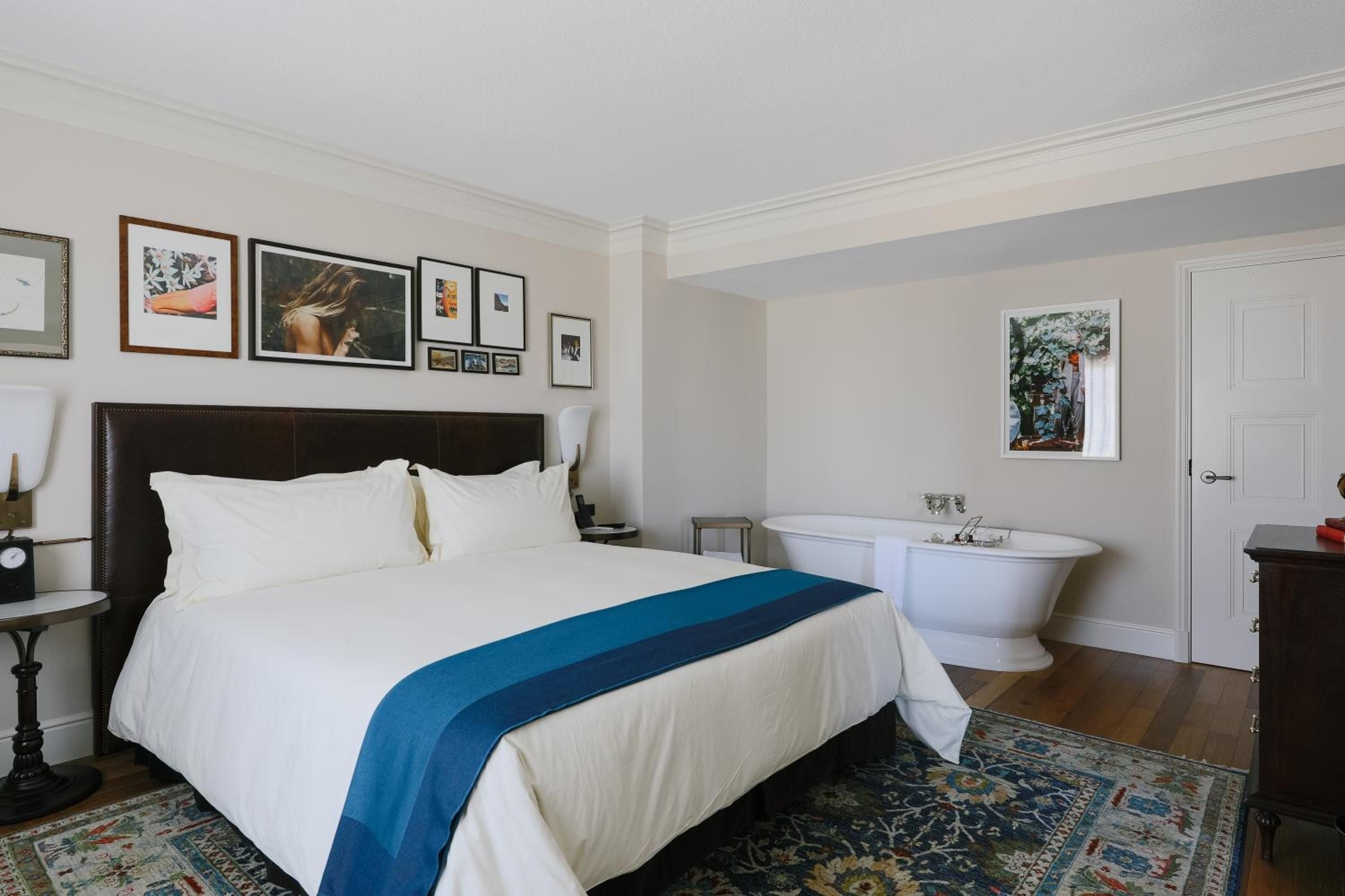 Curated artwork creates an intimate gallery above the leather headboard, while a freestanding soaking tub transforms the bedroom into an unexpected sanctuary of relaxation.