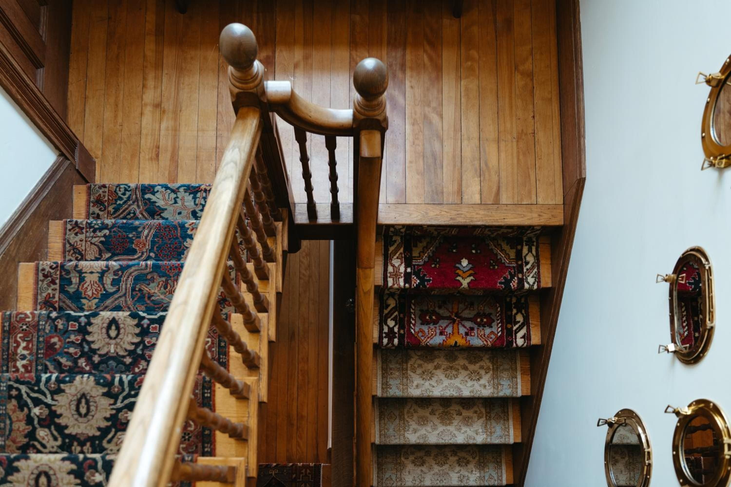 Polished wooden banisters and ornate Persian runners create an elegant ascent, while brass nautical mirrors reflect the inn's maritime heritage along pristine white walls.