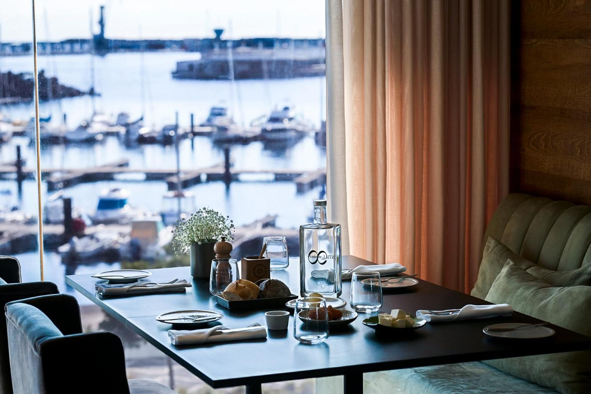 Sunlight streams through floor-to-ceiling windows as breakfast unfolds at waterside tables, framing Ponta Delgada's marina through soft coral curtains and polished surfaces.