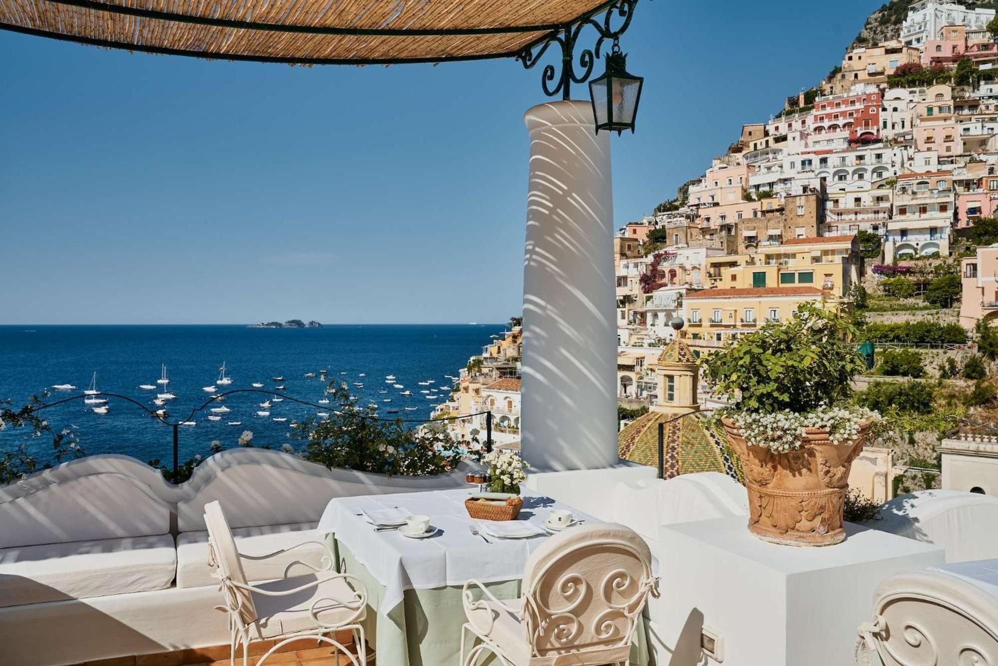 Morning light filters through woven umbrellas onto this intimate terrace, where crisp linens and weathered columns frame Positano's pastel cascade tumbling toward the Mediterranean.