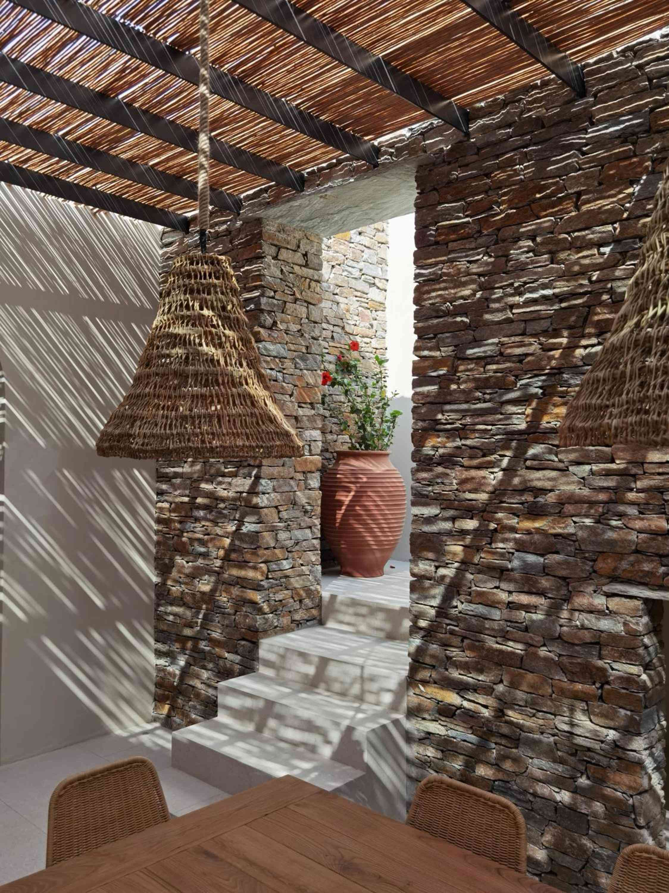 Woven pendant lights cast intricate shadows across stone archways, where terracotta vessels and climbing roses create an intimate Mediterranean courtyard atmosphere.