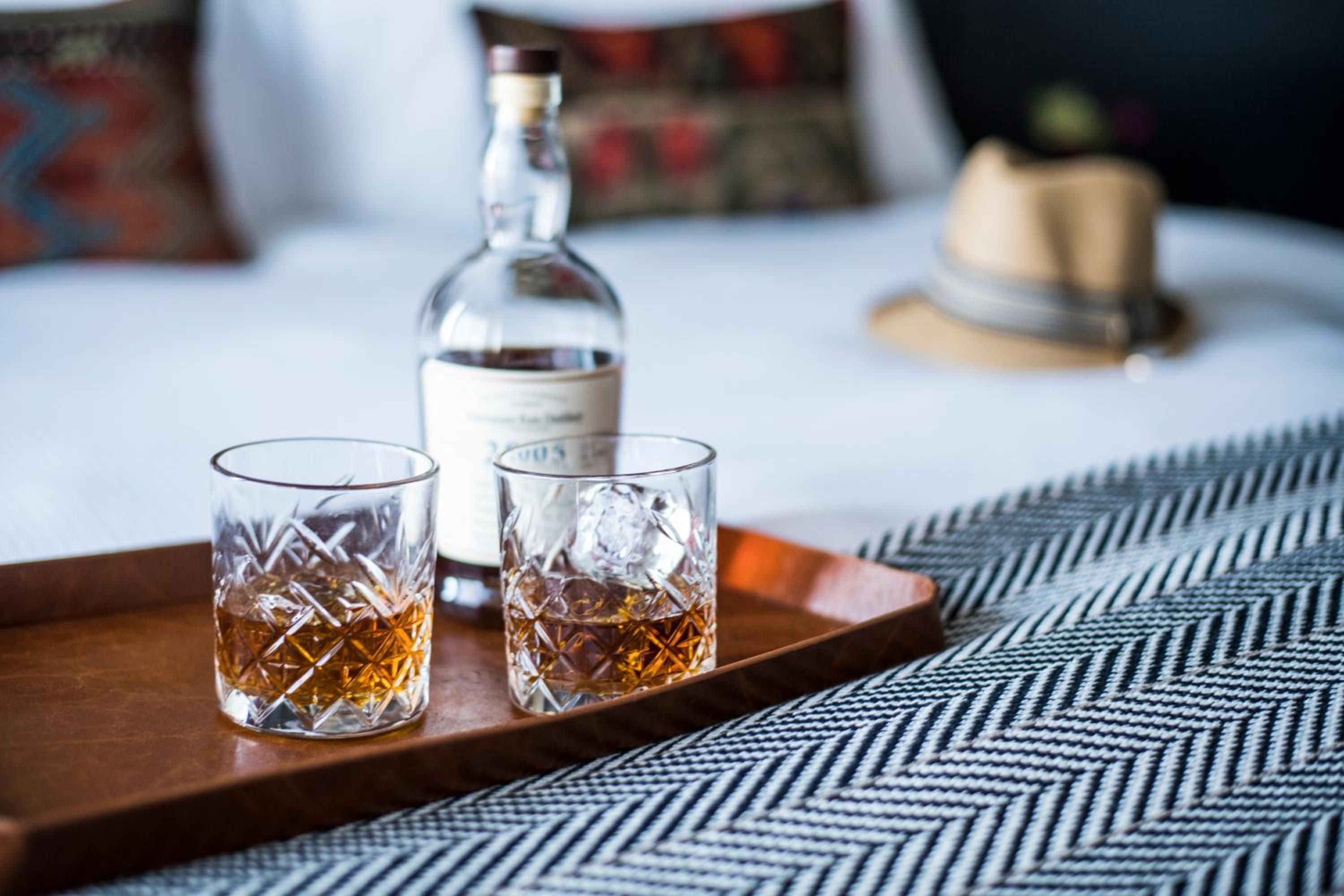 Crystal-cut glasses catch amber light on walnut serving trays, where premium spirits await in an intimate setting of herringbone textiles and warm hospitality.