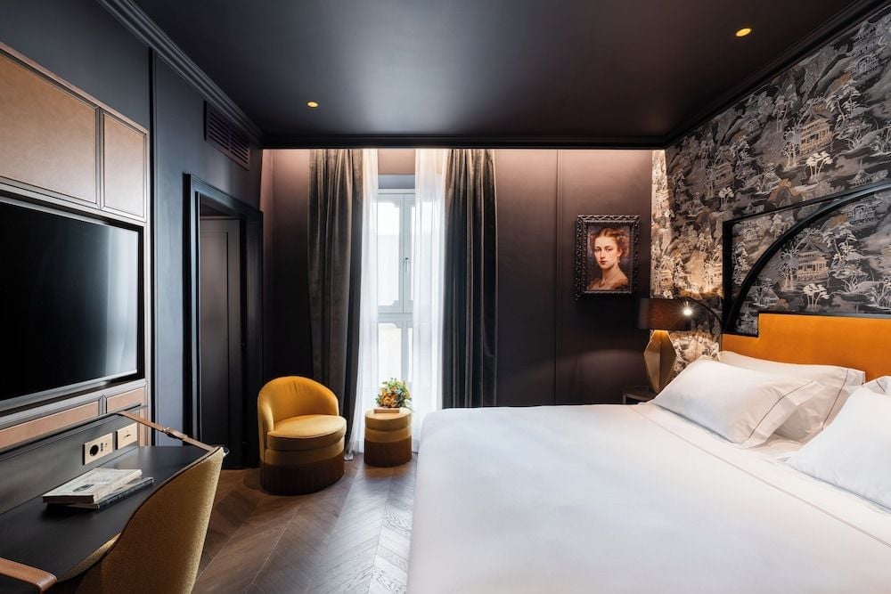 Moody sophistication defines this cocoon-like retreat, where charcoal walls meet toile wallpaper and mustard velvet seating creates intimate warmth against classical portraiture.