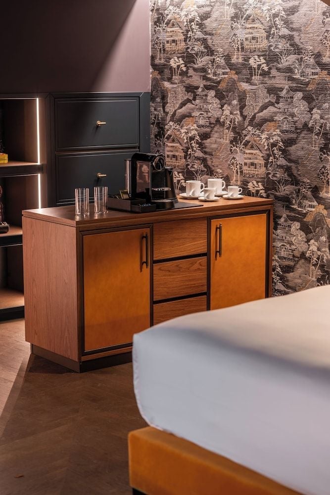 Warm wood credenza and distinctive toile wallpaper create an intimate coffee station where mid-century design meets sophisticated European sensibility in this thoughtfully appointed guest room.