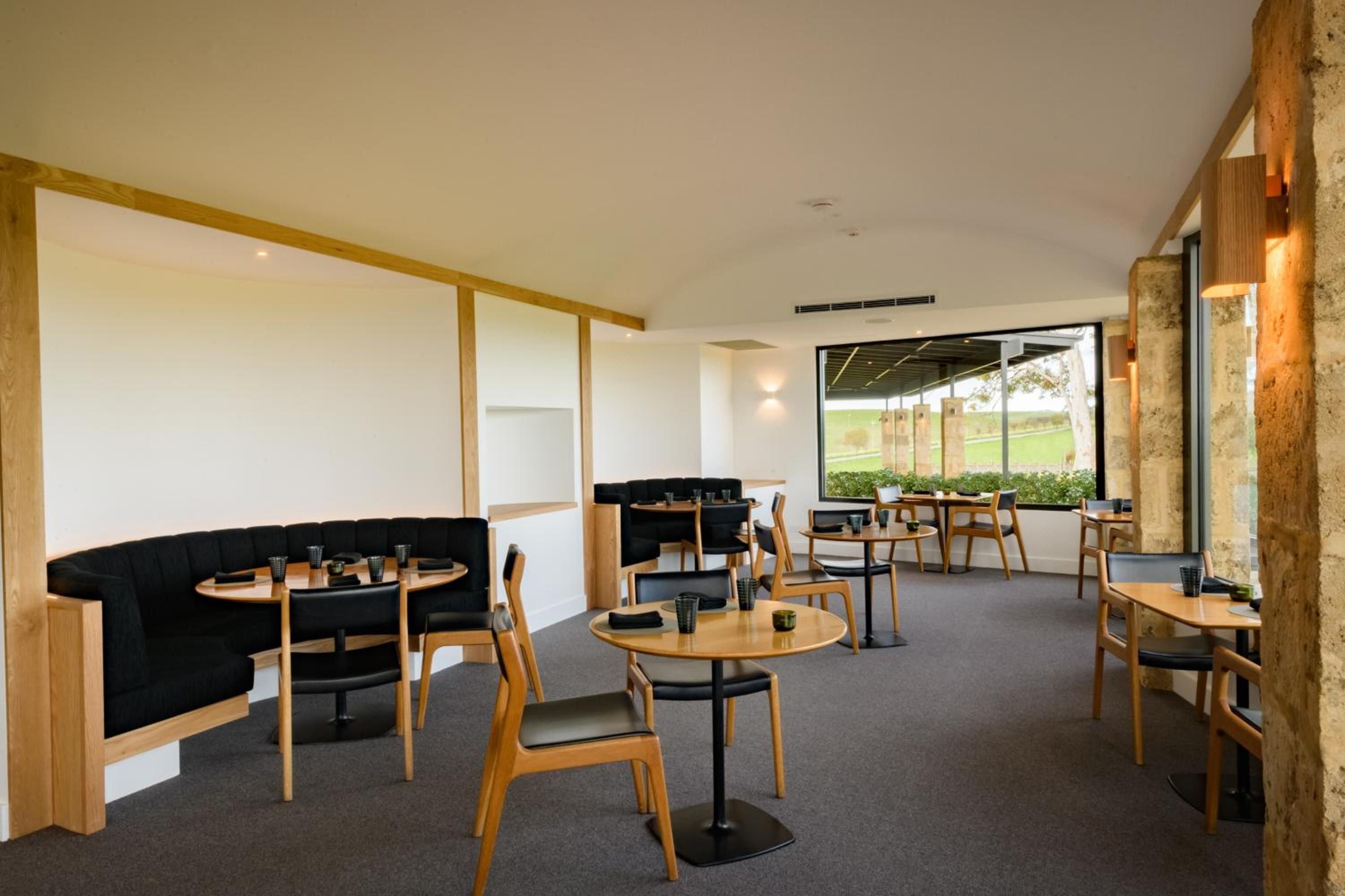 Natural timber frames and charcoal banquettes create intimate dining nooks, while vineyard views through floor-to-ceiling windows remind guests they're dining in Barossa Valley wine country.