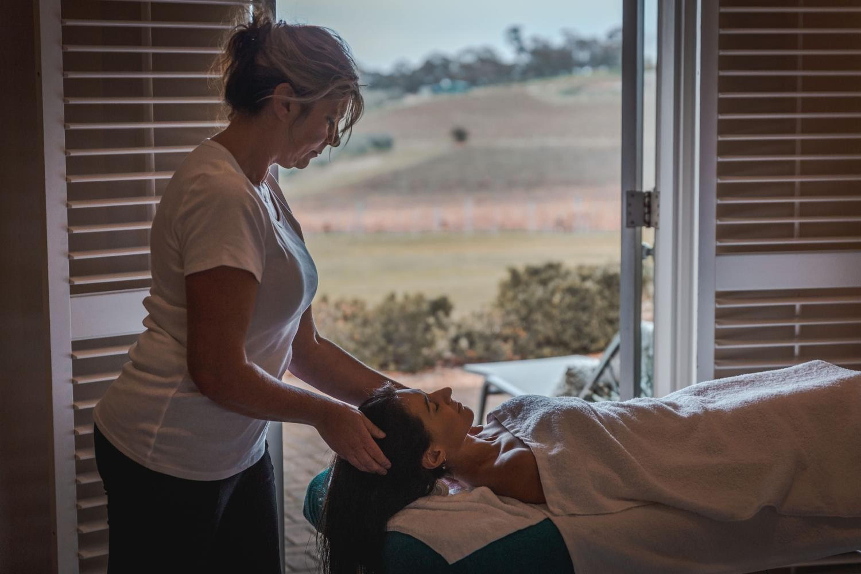 Warm afternoon light streams through plantation shutters as expert hands work their magic, the rolling Barossa Valley vineyards creating a serene backdrop for pure indulgence.