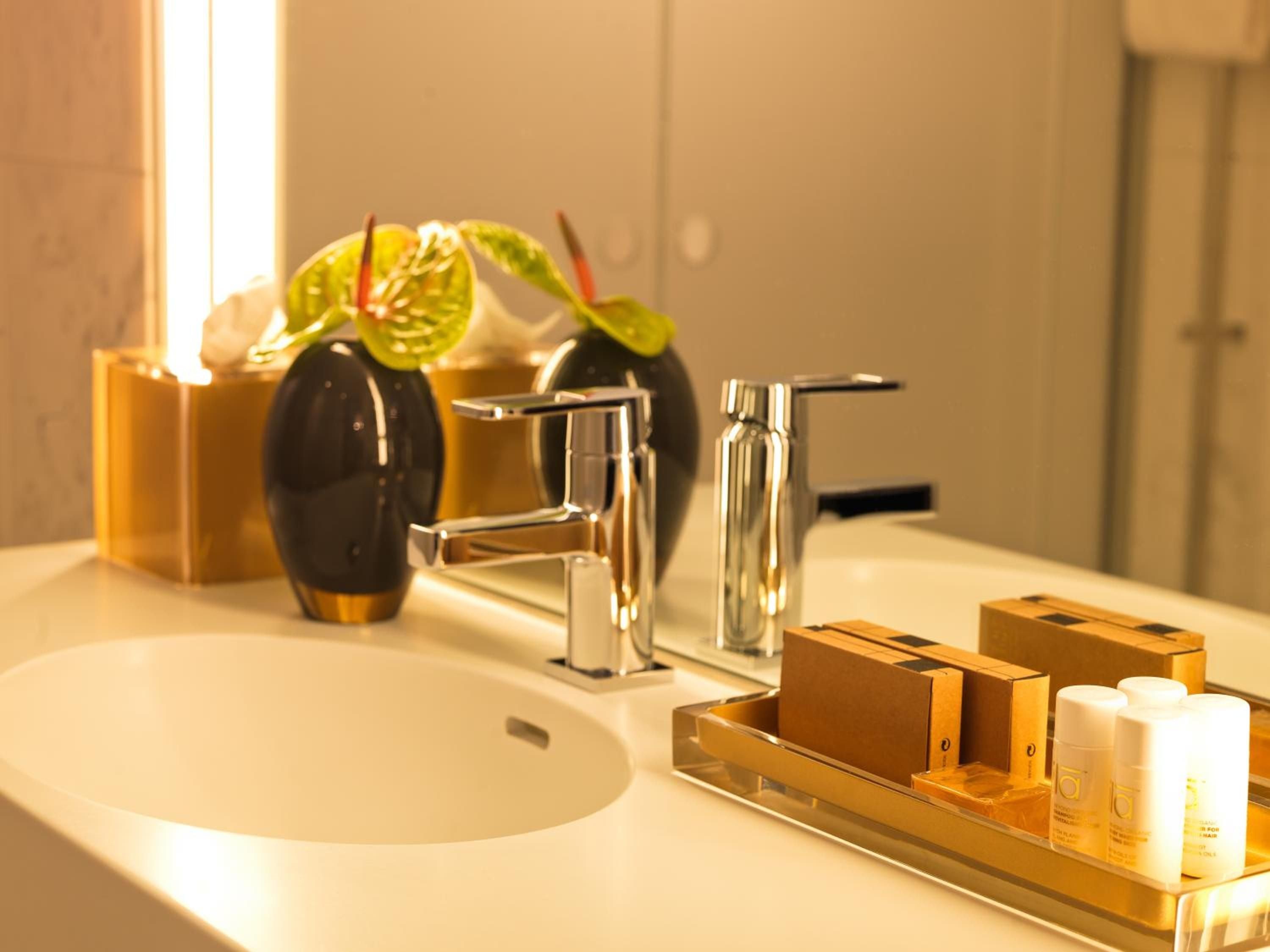Chrome fixtures gleam against warm marble while curated amenities and fresh anthurium blooms transform the vanity into a study in Scandinavian luxury.