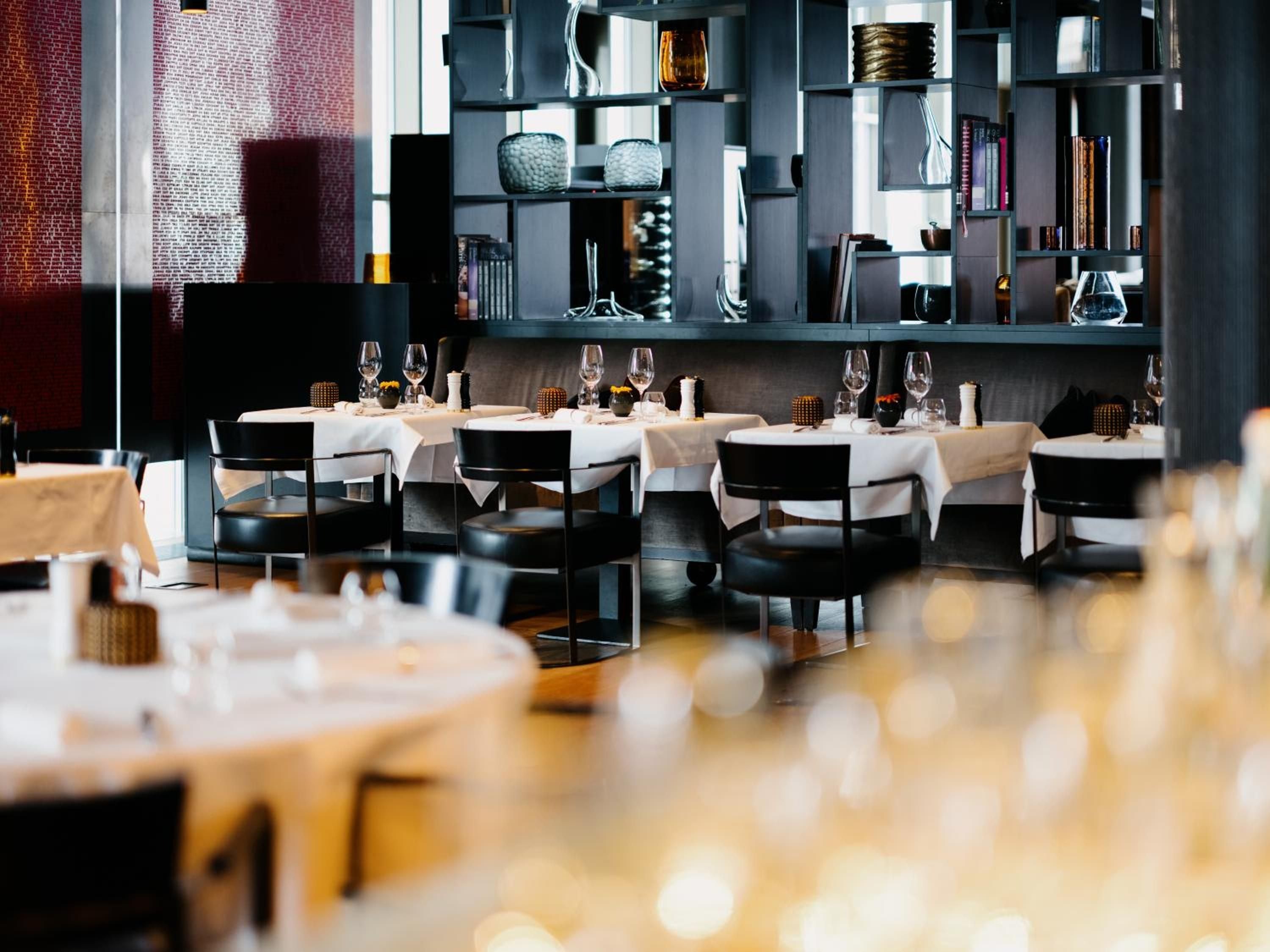 Modern Nordic elegance unfolds in the hotel's signature restaurant, where geometric shelving displays art objects above pristinely set tables bathed in golden afternoon light.