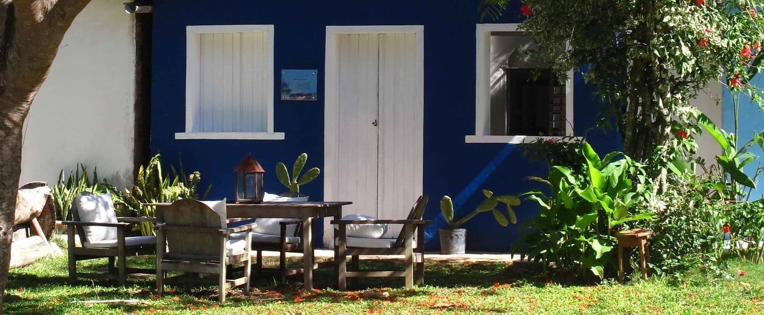 Rustic wooden chairs beckon beneath swaying palms, where cobalt walls and weathered shutters frame an intimate courtyard sanctuary dotted with tropical plantings.