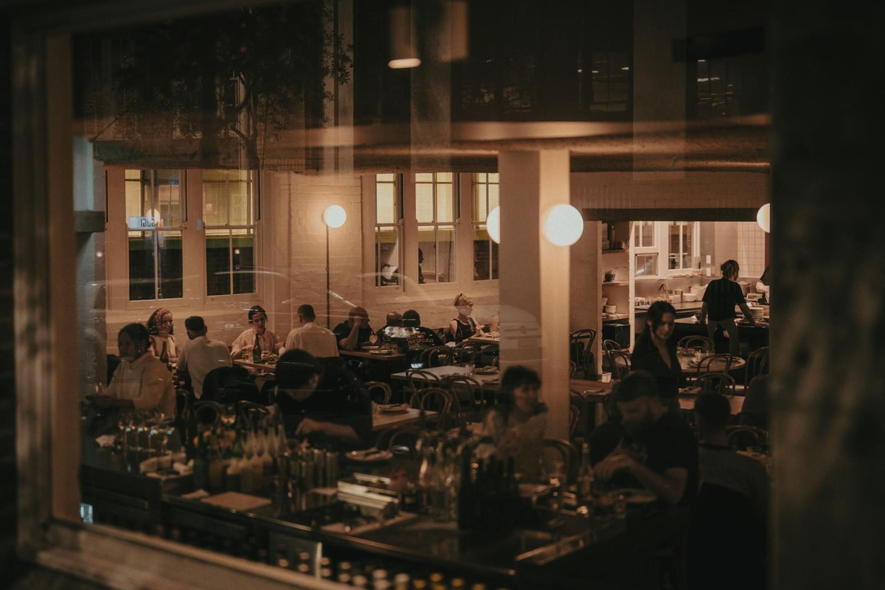Golden light spills across bentwood chairs and marble surfaces as diners gather in the hotel's inviting restaurant, where warm industrial touches create intimate evening conversations.