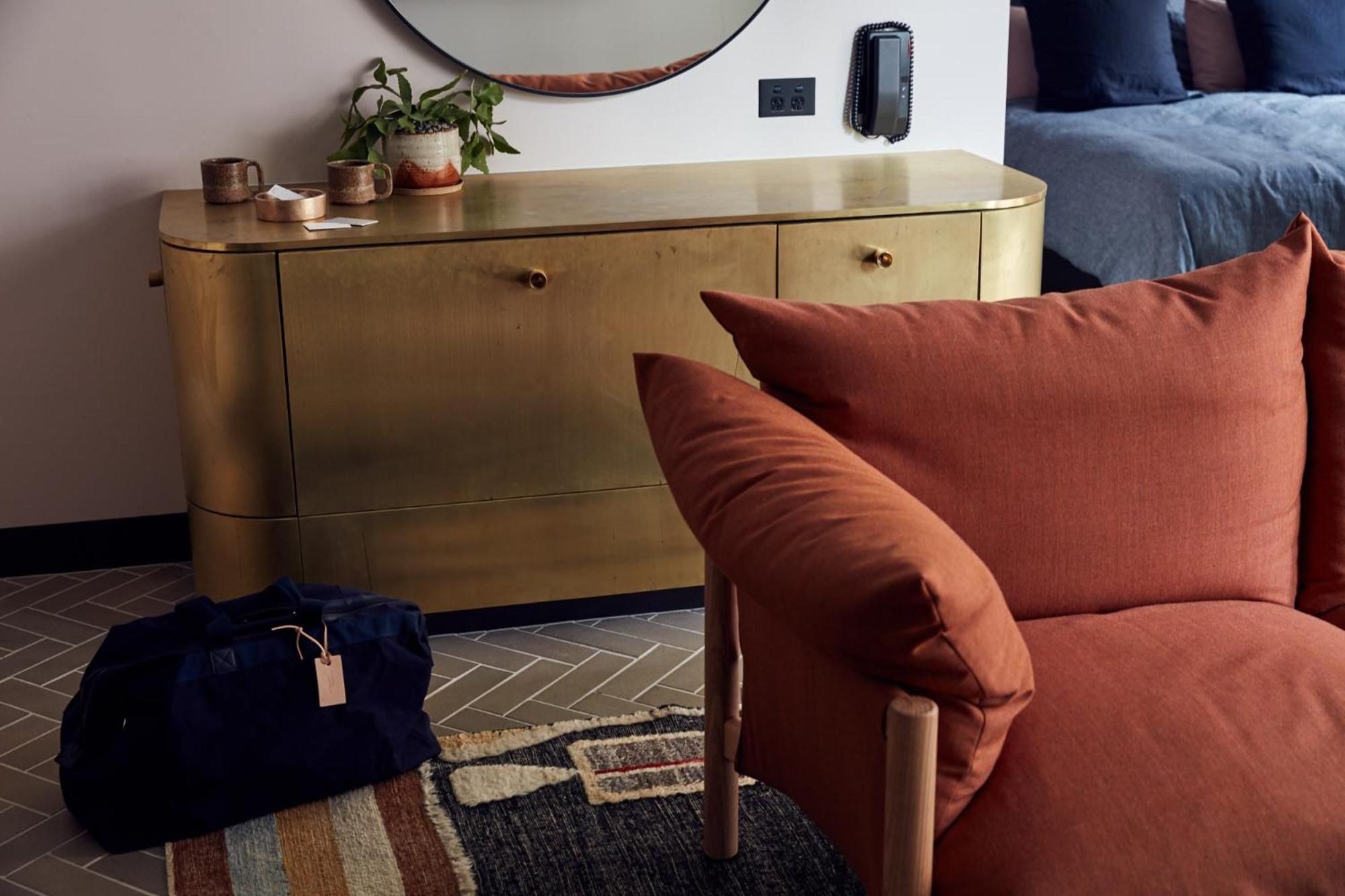 Warm terracotta cushions and brass accents create an intimate corner where mid-century elegance meets contemporary comfort in thoughtfully curated guest quarters.