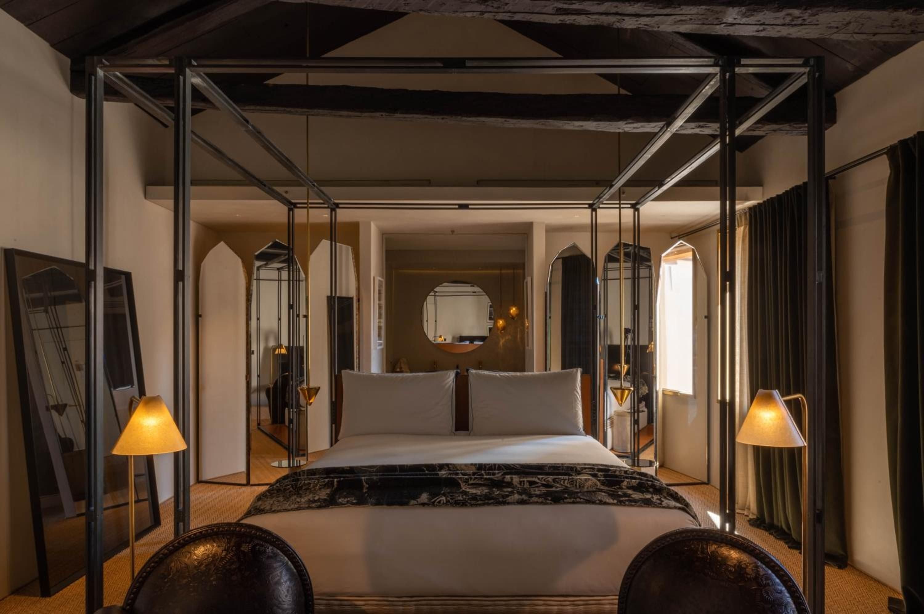 Warm amber light filters through the canopy bed's sleek metal frame, where exposed beams meet modern luxury in this atmospheric suite overlooking Venetian waters.