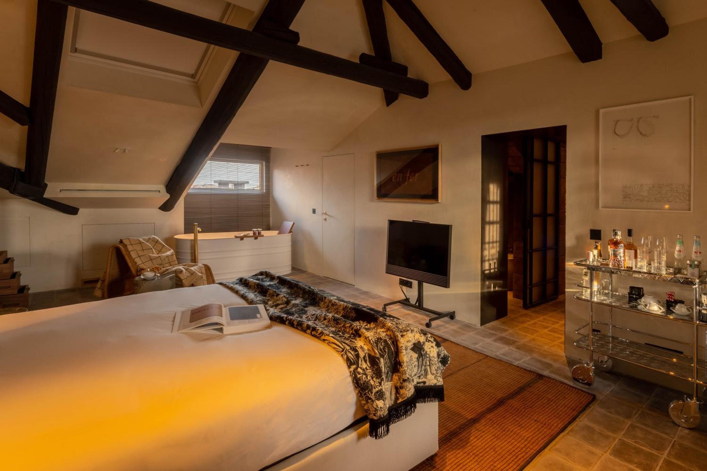 Exposed wooden beams frame this intimate attic suite where contemporary luxury meets Venetian charm, complete with soaking tub and well-stocked bar cart.