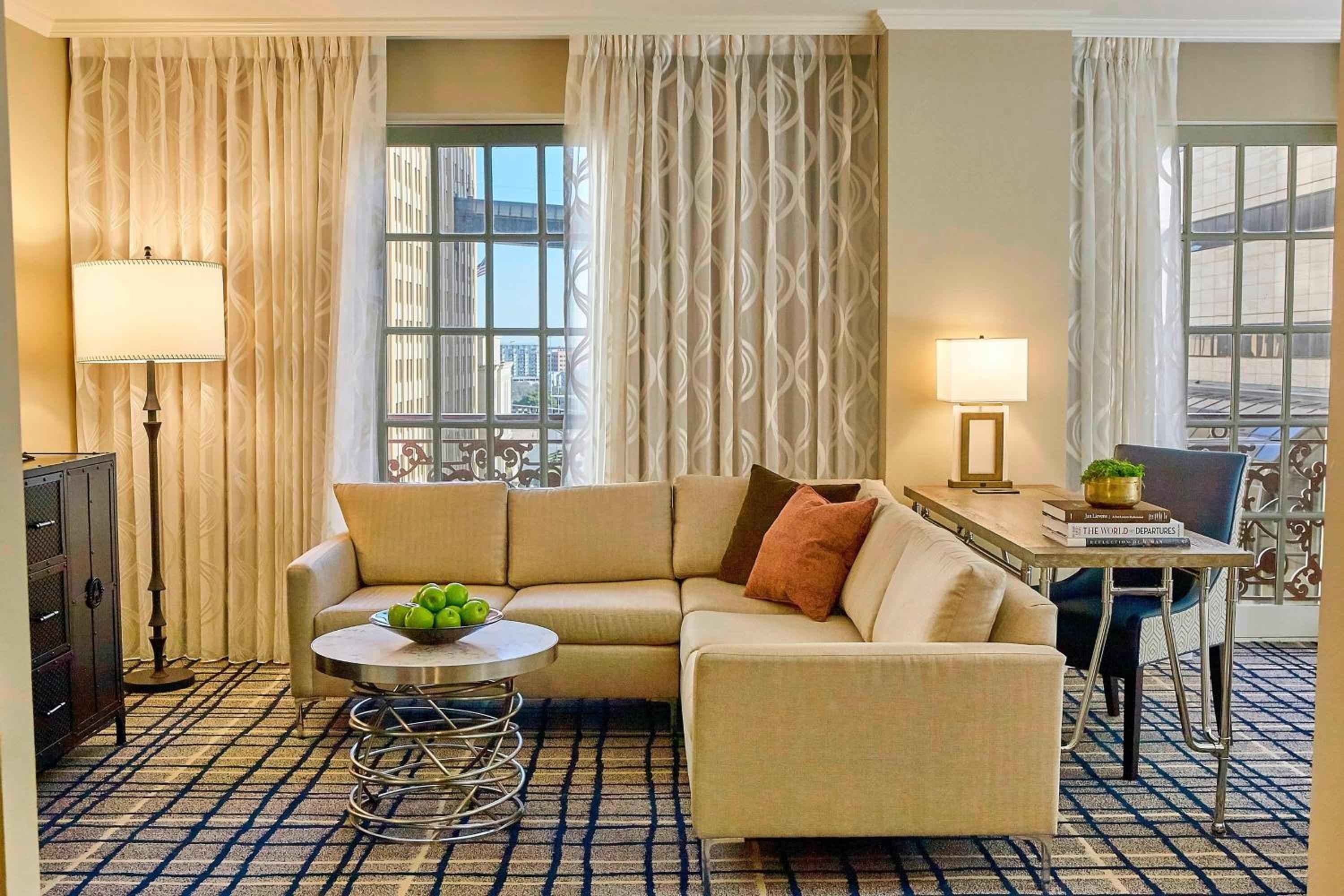 Plush sectional seating and geometric curtains frame downtown views in this sophisticated suite, where warm lighting and rich textures create an inviting urban retreat.