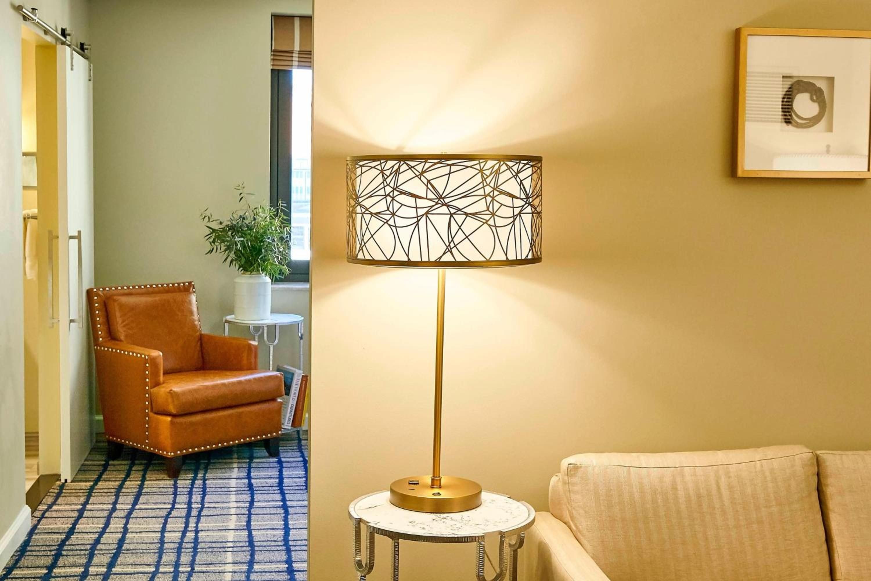 Warm brass lighting and cognac leather create an intimate reading nook, where geometric lampshades cast intricate shadows across cream walls and striped rugs invite quiet contemplation.