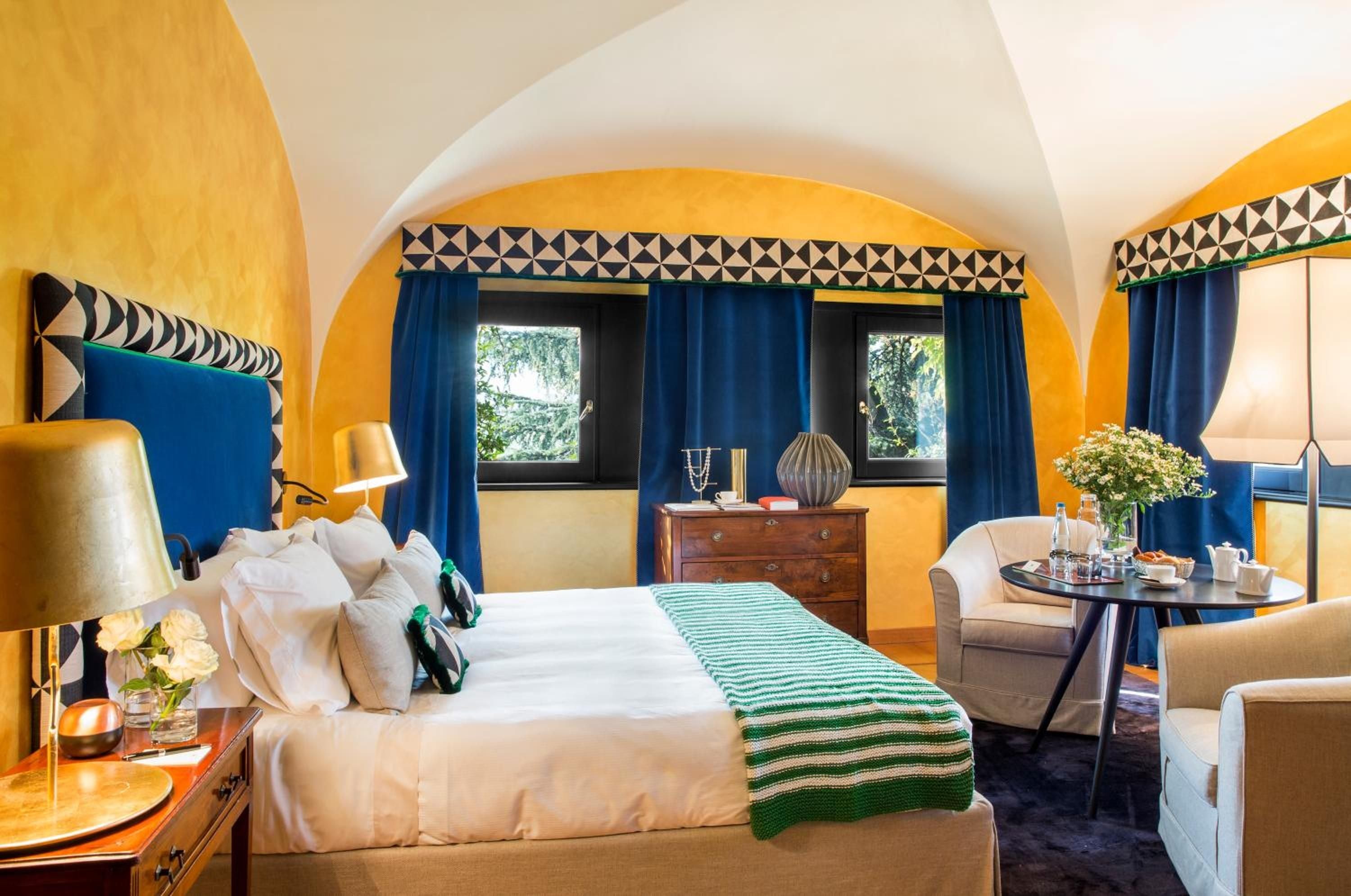 Vibrant cobalt and golden ochre embrace guests in this distinctive suite, where geometric patterns and arched windows frame rolling vineyard views beyond silk curtains.