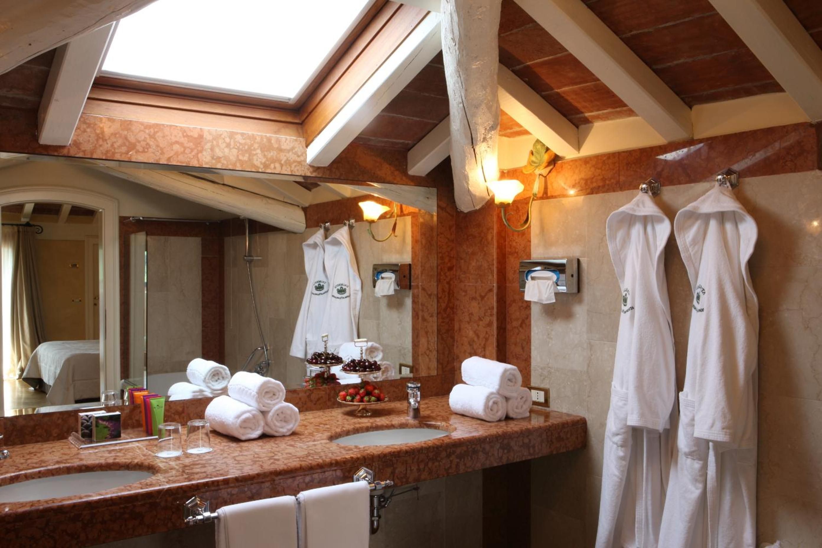 Exposed wooden beams frame a marble vanity where fluffy robes await, while skylights bathe the rustic-luxe bathroom in golden Italian light.