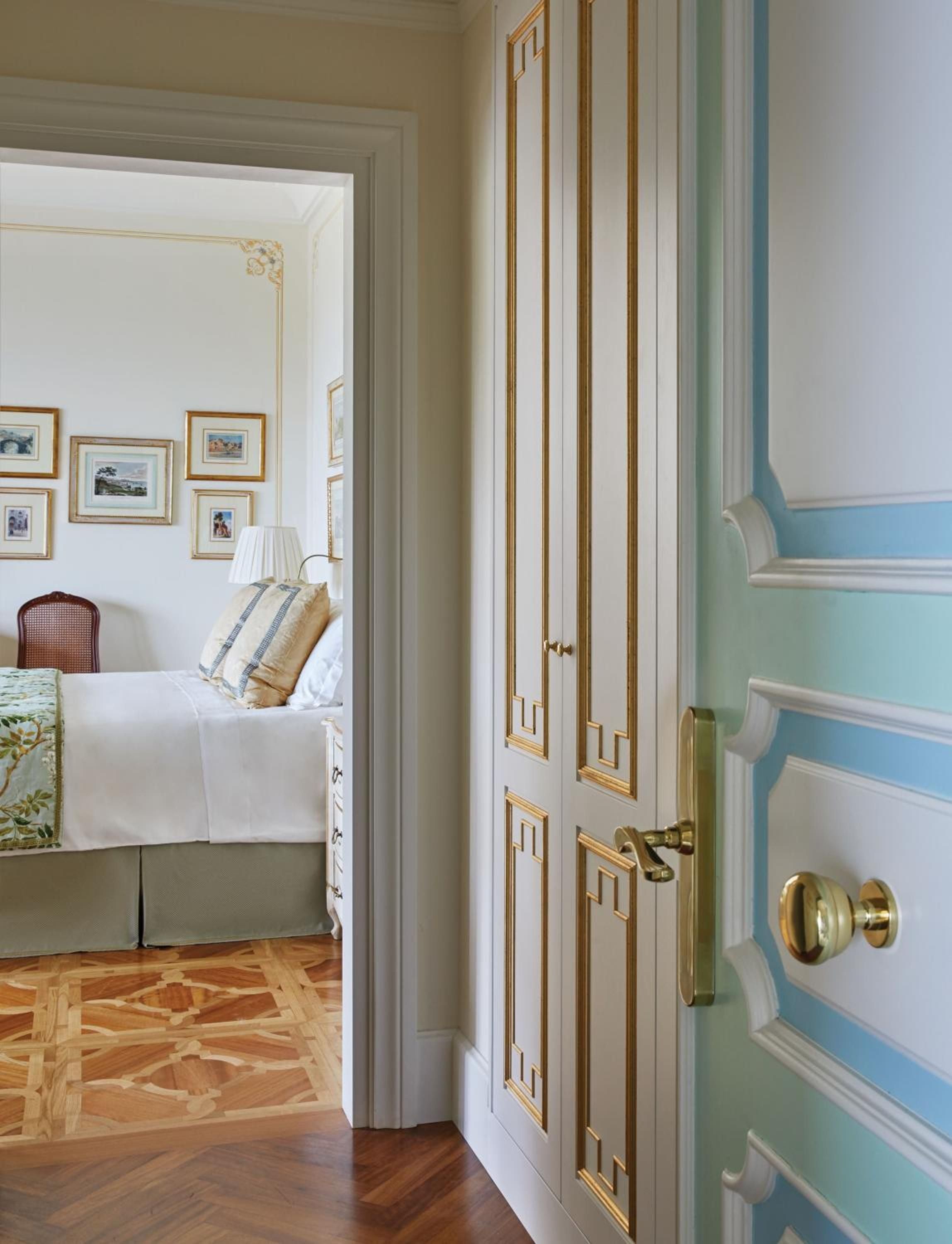 Soft blue walls and gold-trimmed doors frame the entrance to elegantly appointed guest quarters, where parquet floors gleam beneath thoughtfully curated artwork.