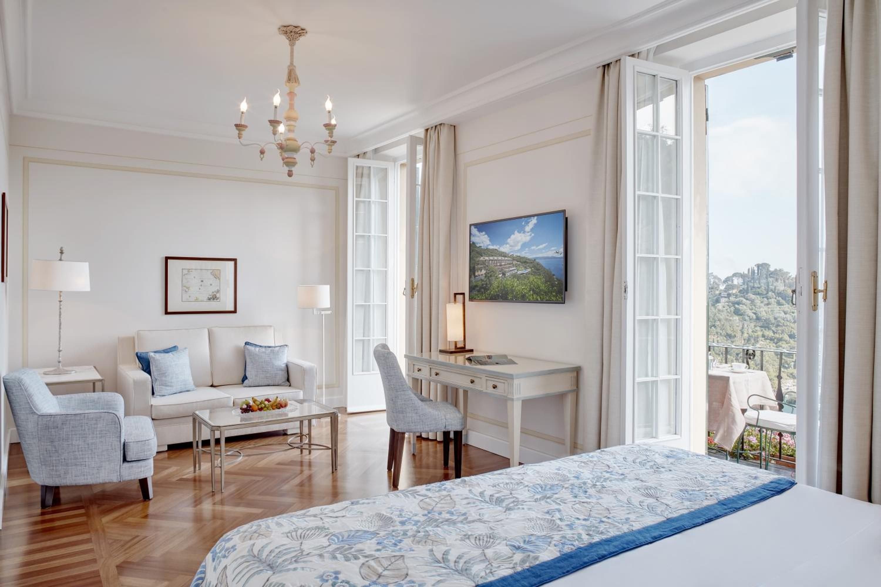 Crisp white linens and polished parquet floors create serene elegance, while French doors frame sweeping views of the Ligurian coastline beyond.