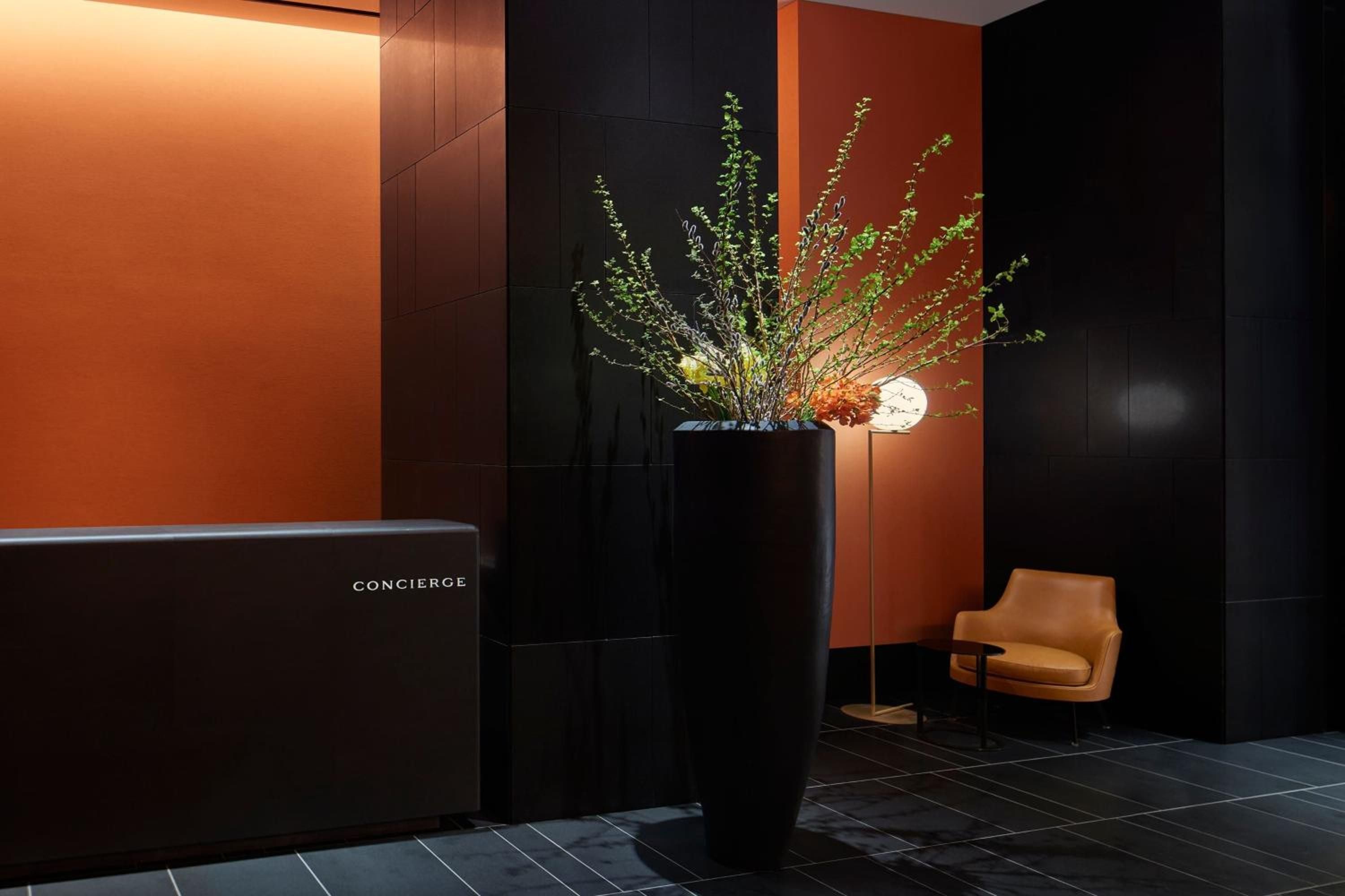 Sleek black marble surfaces meet warm amber lighting at the concierge desk, where minimalist design creates an intimate atmosphere of sophisticated luxury.