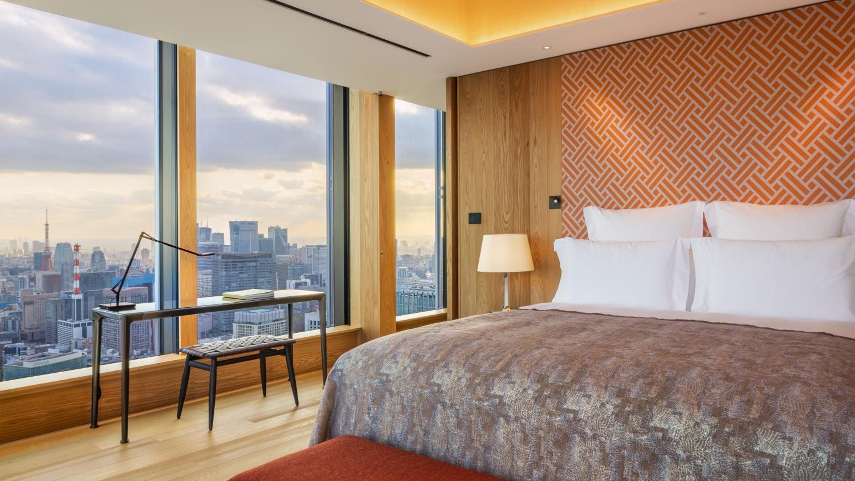 Floor-to-ceiling windows frame Tokyo's glittering skyline while warm wood tones and geometric patterns create an intimate sanctuary high above the urban sprawl.