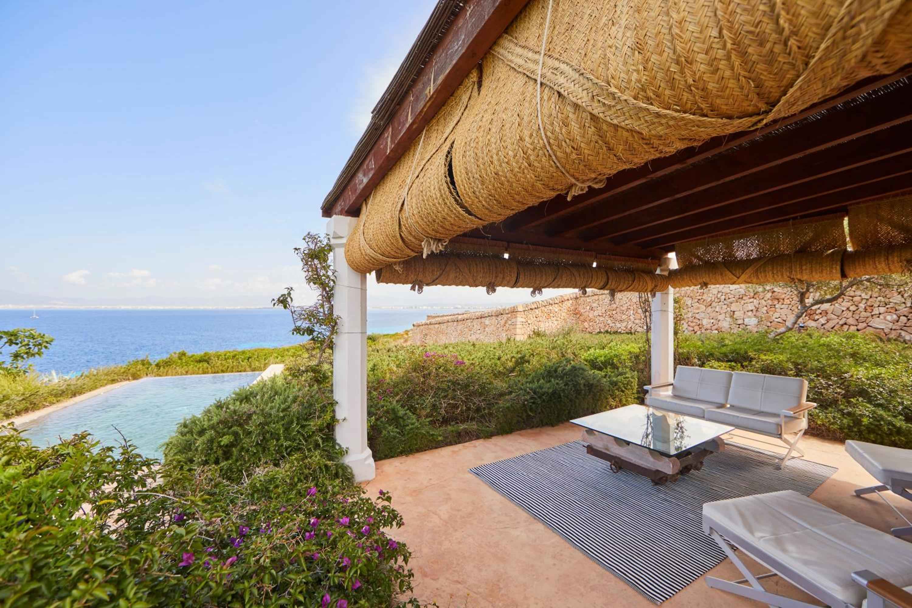 Woven reed canopies filter Mediterranean light across this clifftop terrace, where infinity pool meets endless blue horizon and ancient stone walls frame the Mallorcan coastline.