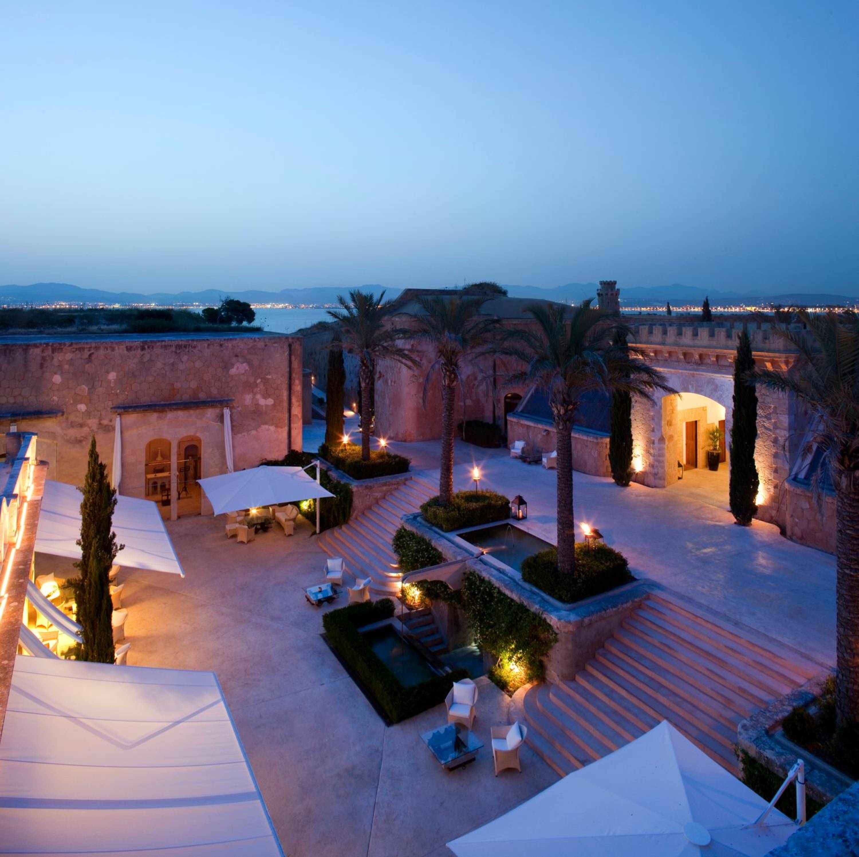 Stone terraces cascade beneath twilight skies, where palm fronds whisper against honey-lit walls and the Mediterranean stretches endlessly beyond this clifftop fortress.