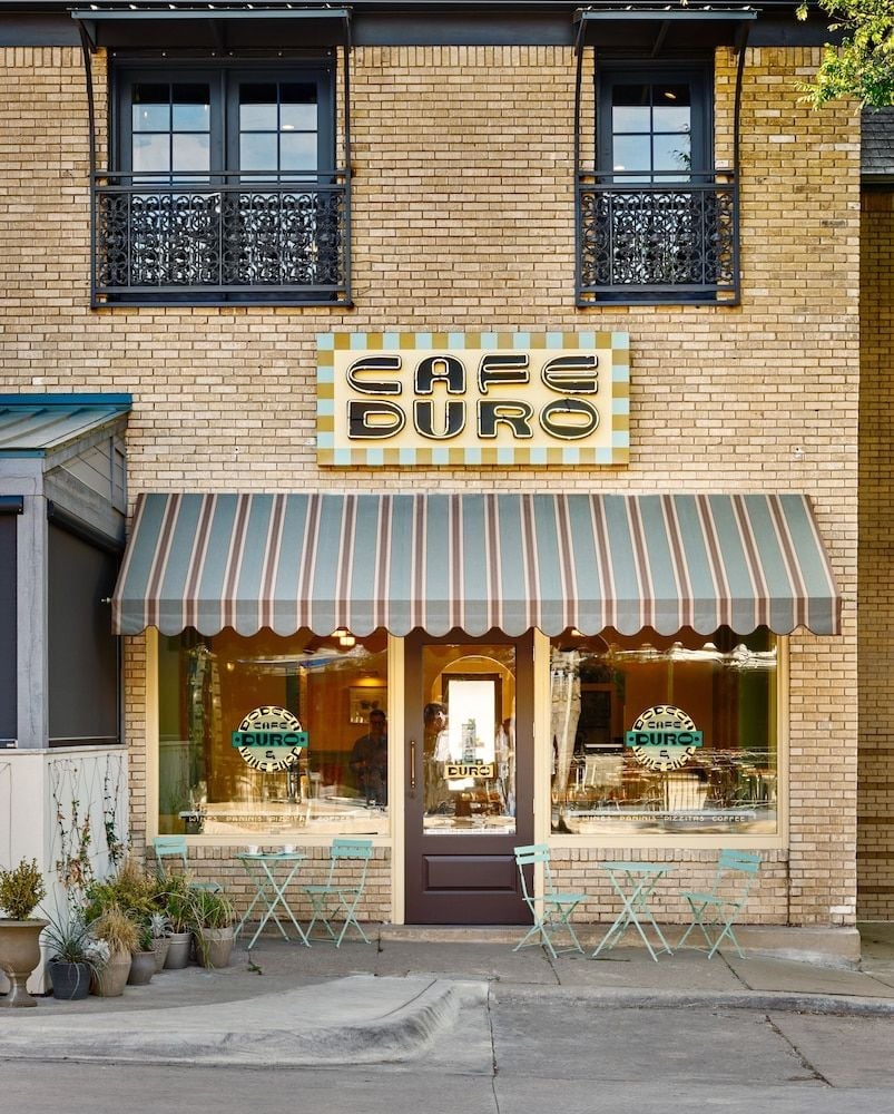 Striped awnings and bistro tables create European charm at this neighborhood café, where warm brick façades and ornate balconies frame intimate sidewalk dining beneath golden afternoon light.