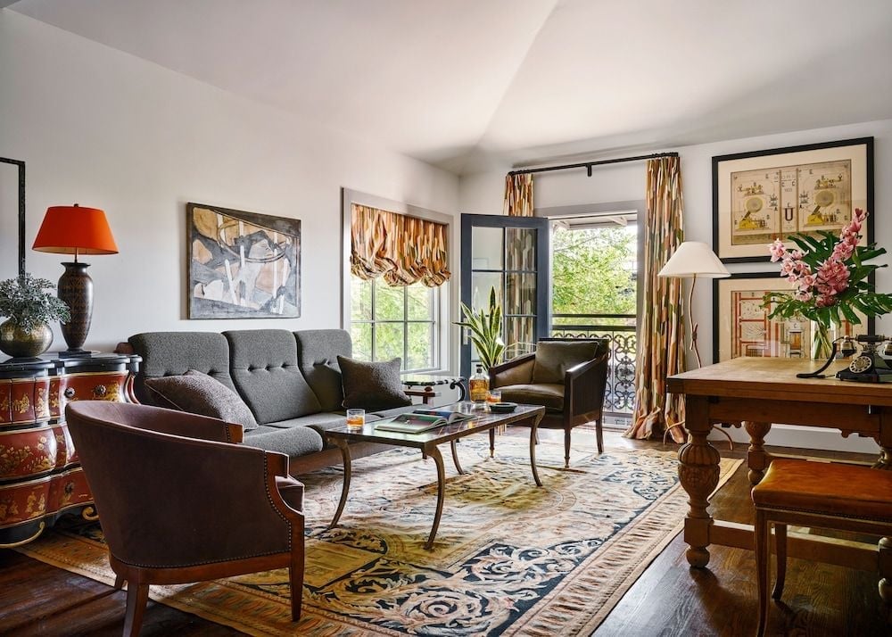 Sunlight filters through French doors into this elegantly appointed sitting room, where vintage botanicals and golden curtains create an intimate retreat overlooking verdant gardens.