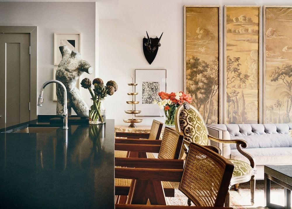 Antique cane chairs gather around polished wood while golden chinoiserie panels frame a tufted banquette, creating an intimate dining corner where old-world elegance meets contemporary sophistication.