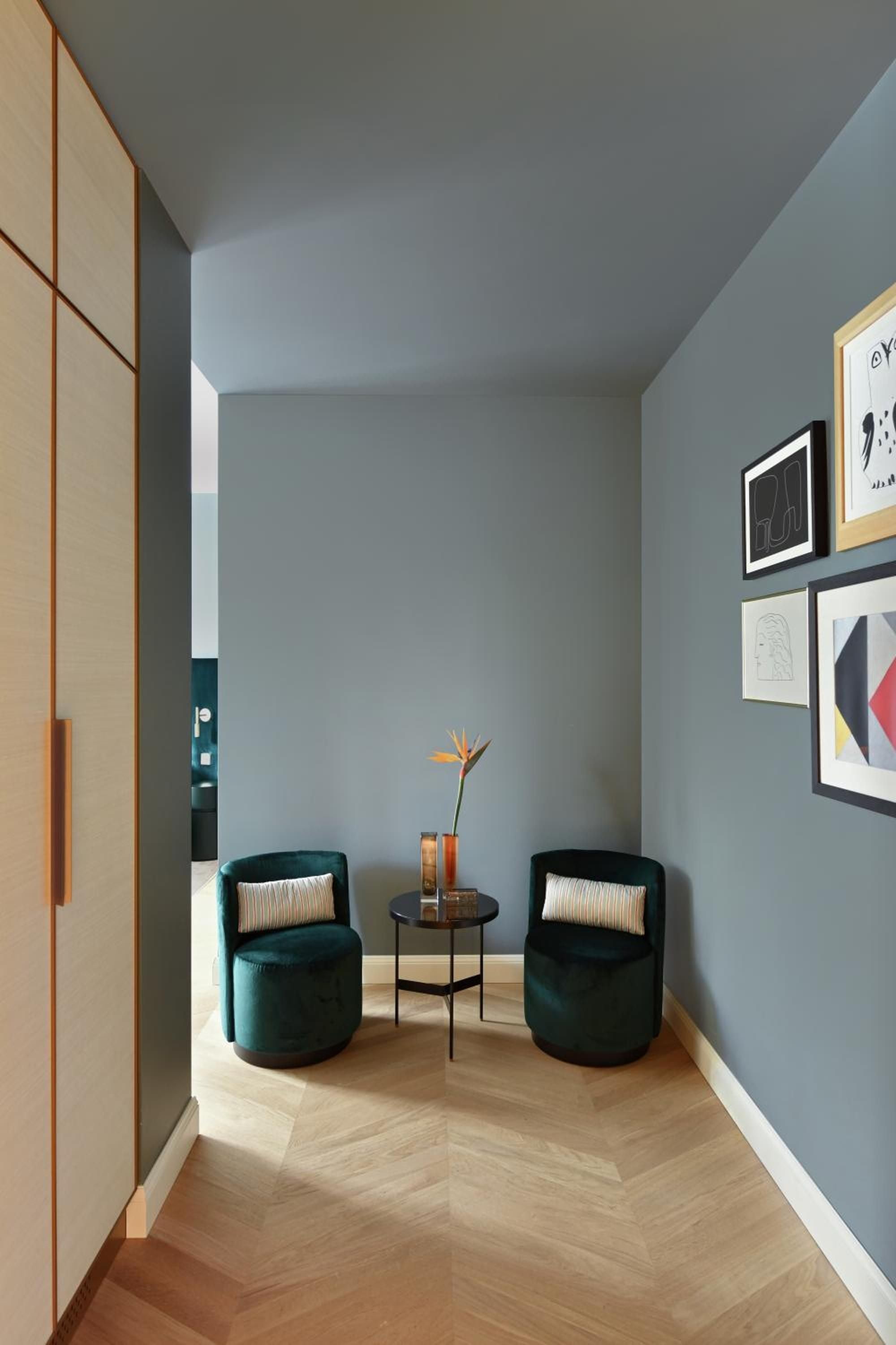 Emerald velvet chairs frame intimate conversations in this sophisticated nook, where herringbone floors meet gallery walls and mid-century elegance defines every carefully curated corner.