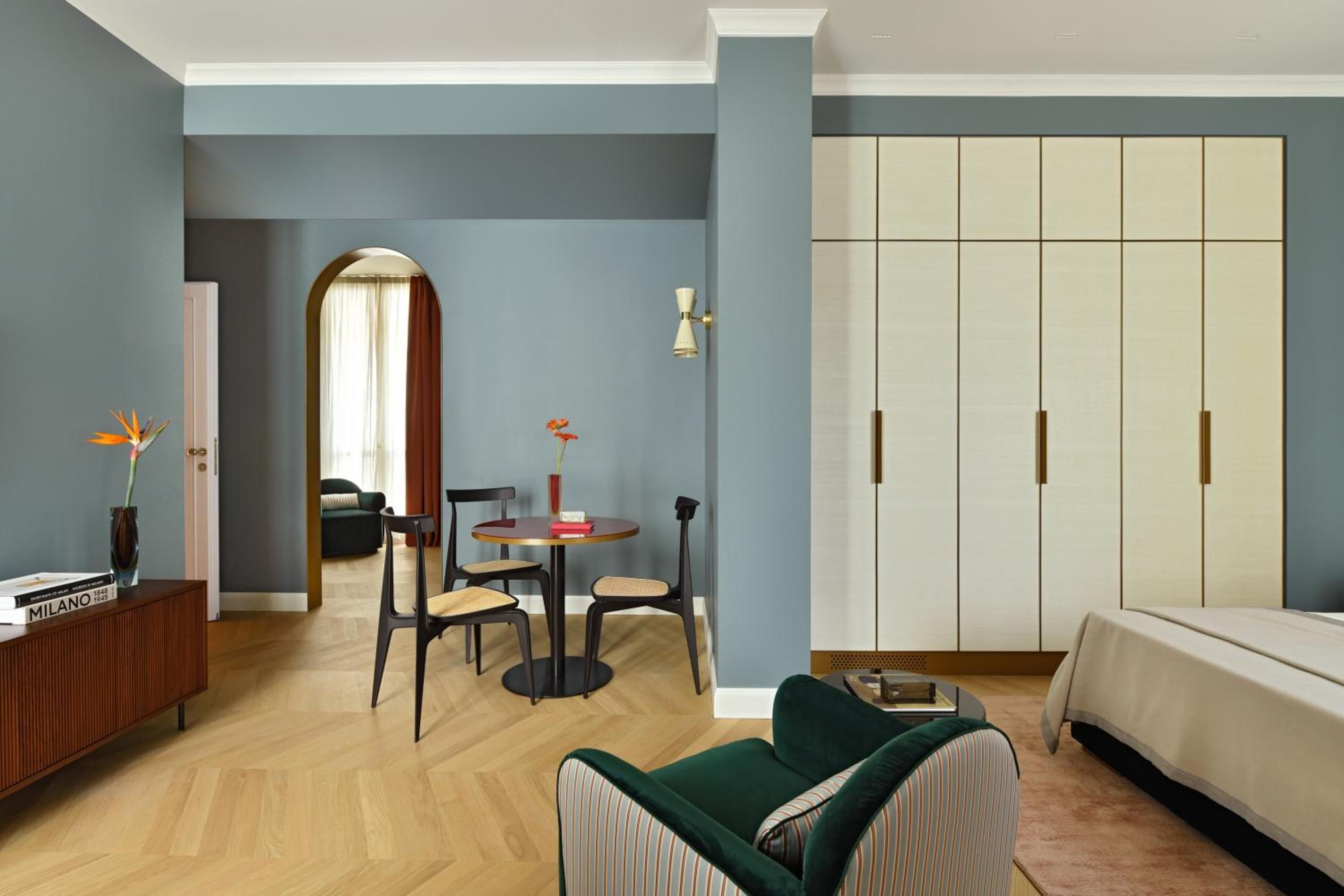 Sage-hued walls frame a thoughtfully curated space where mid-century dining chairs meet emerald velvet seating, creating an intimate sanctuary bathed in natural light.