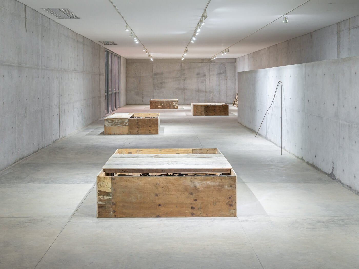 Raw concrete walls frame weathered wooden crates in Casa Wabi's contemplative gallery space, where track lighting illuminates art installations with museum-quality precision.