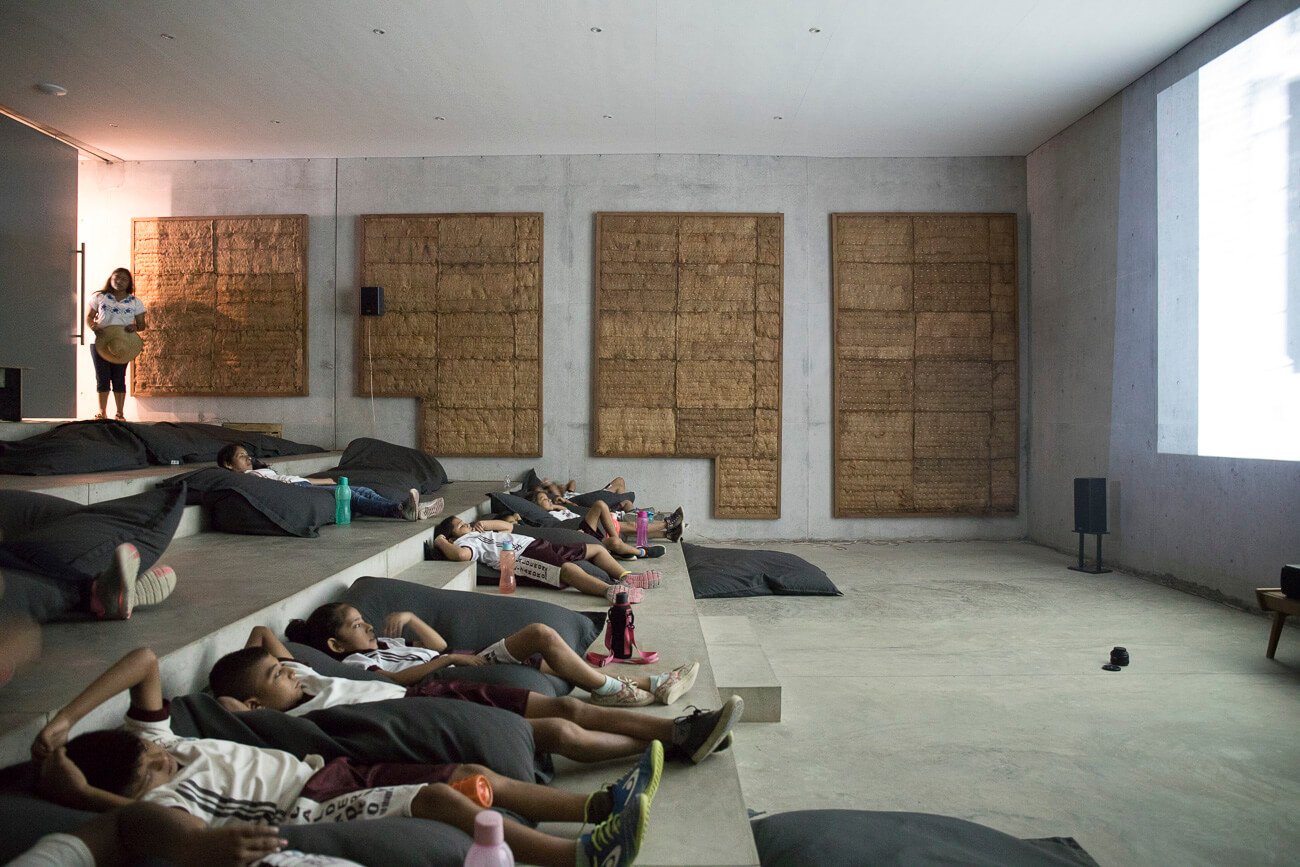 Athletes recover in Casa Wabi's minimalist meditation hall, where woven palm panels and concrete create a serene sanctuary bathed in golden afternoon light.