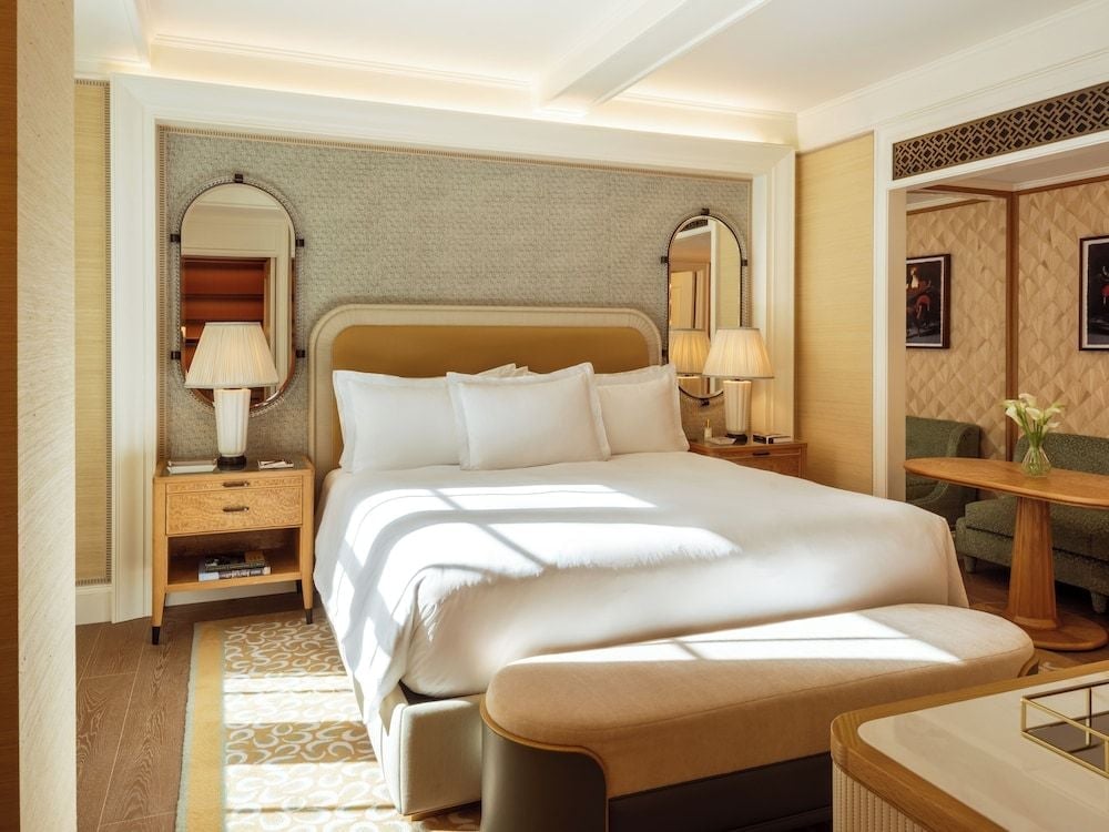 Sunlight streams across crisp white linens in this sophisticated guest room, where warm wood furnishings and geometric patterns create an inviting Upper East Side sanctuary.