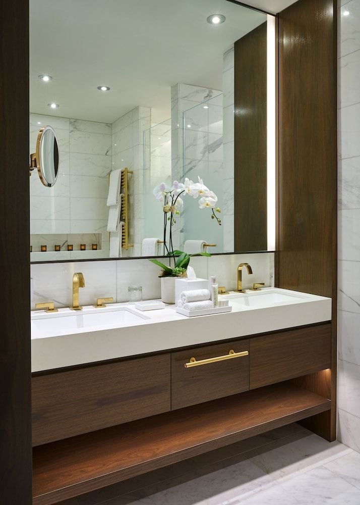 Warm walnut vanities and brass fixtures create an intimate sophistication, while white orchids add a delicate touch to the spa-like marble sanctuary.
