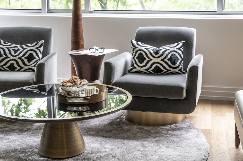 Swivel chairs in dove-gray velvet invite conversation beside brass-accented tables, where geometric pillows add graphic punch to this sophisticated seating area.