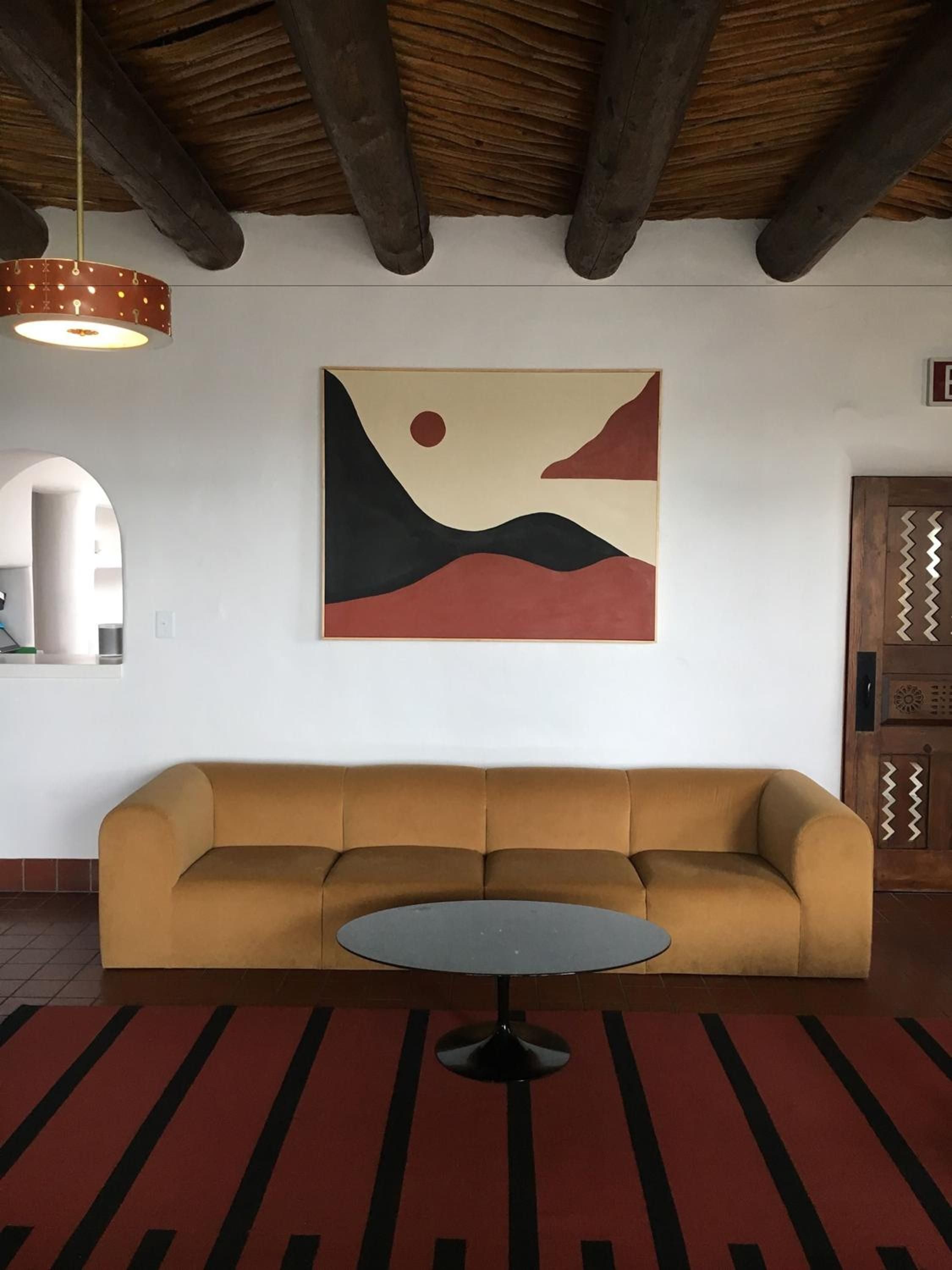 Exposed wooden beams frame a mid-century modern lounge where geometric art and mustard velvet create an unexpectedly sophisticated refuge in this reimagined motor lodge.