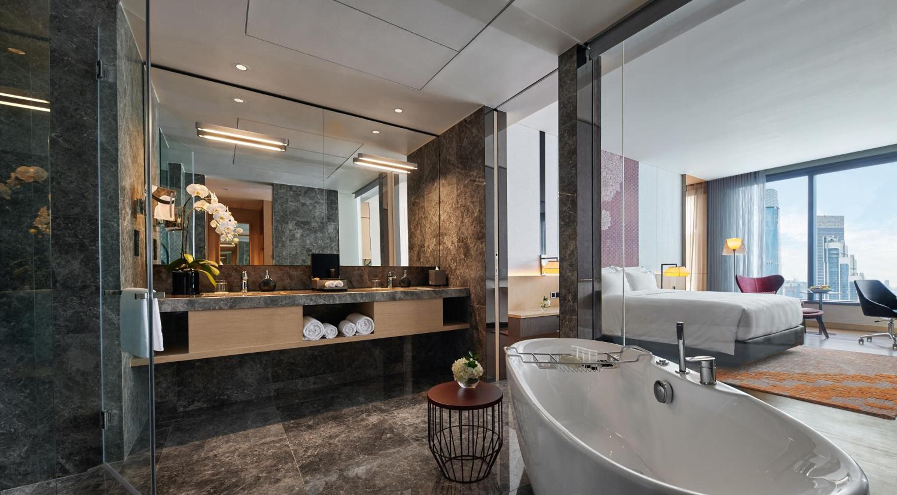 Dark marble and warm wood create an intimate sanctuary where the freestanding tub offers front-row seats to Kuala Lumpur's glittering skyline through floor-to-ceiling windows.