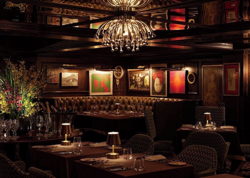 Intimate dining unfolds beneath dramatic chandeliers where eclectic contemporary art punctuates rich leather banquettes and warm wood paneling in this sophisticated Palm Springs sanctuary.