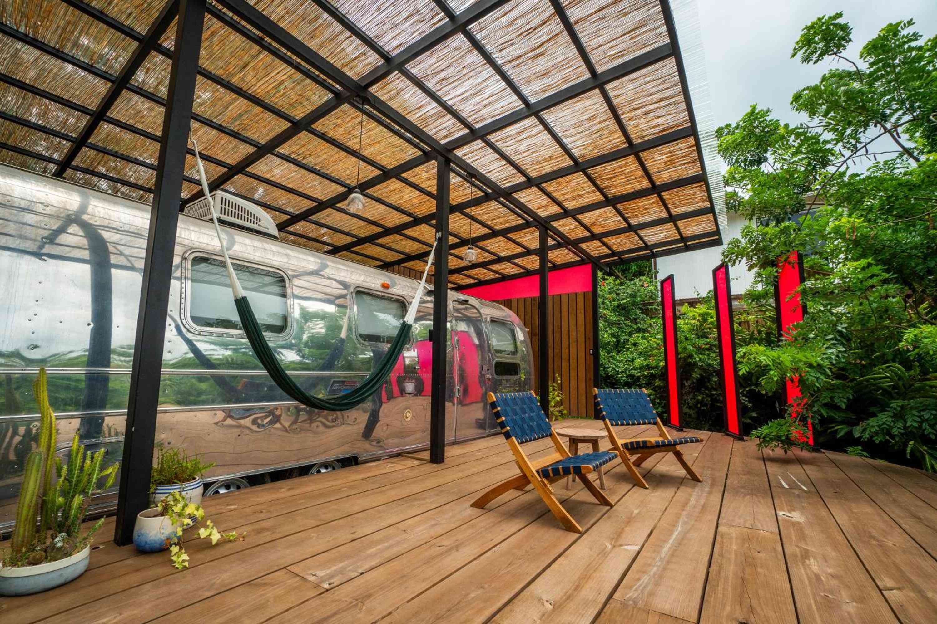 Vintage Airstream trailers find new purpose as glamping accommodations, sheltered beneath bamboo-screened pergolas with handwoven lounge chairs positioned for afternoon relaxation.