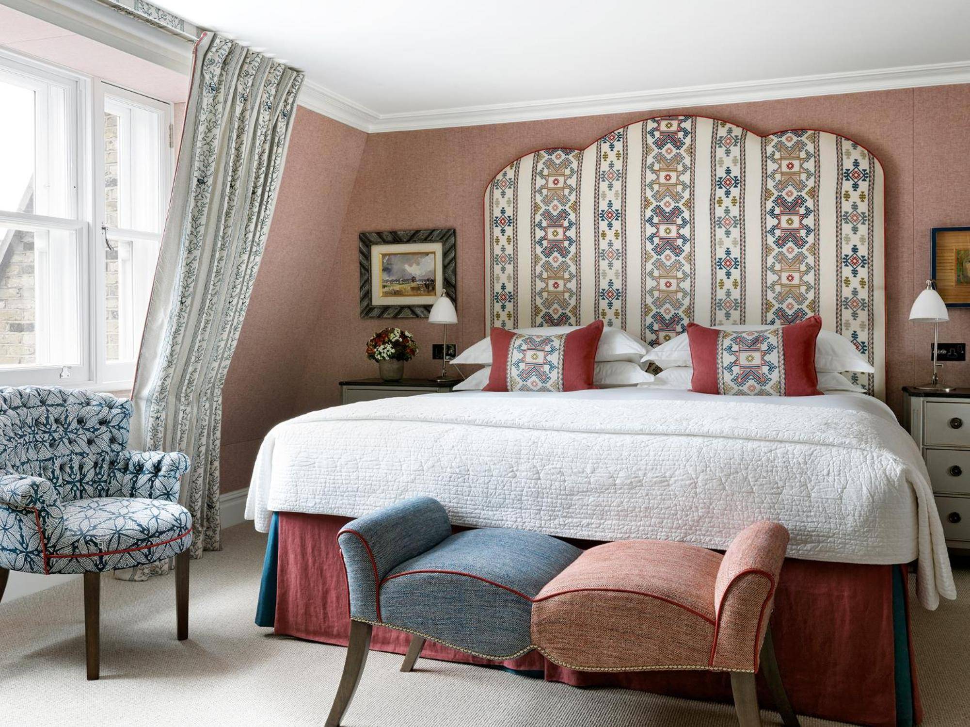 Geometric headboard patterns and dusty rose walls create intimate charm, while the curved bench and patterned armchair invite lingering over morning tea by tall Georgian windows.