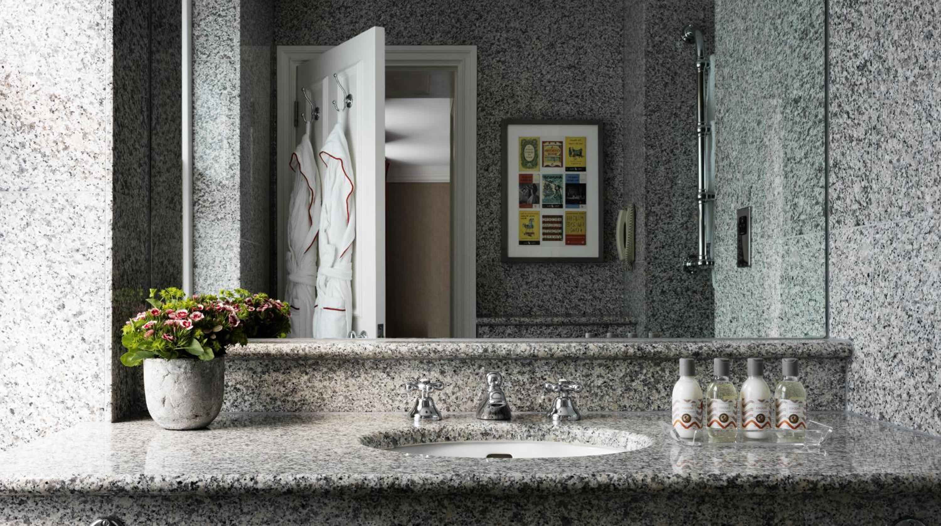 Speckled granite surfaces and chrome fixtures create a sophisticated bathroom retreat, where vintage-inspired amenities and fresh blooms add unexpected warmth to the polished stone palette.