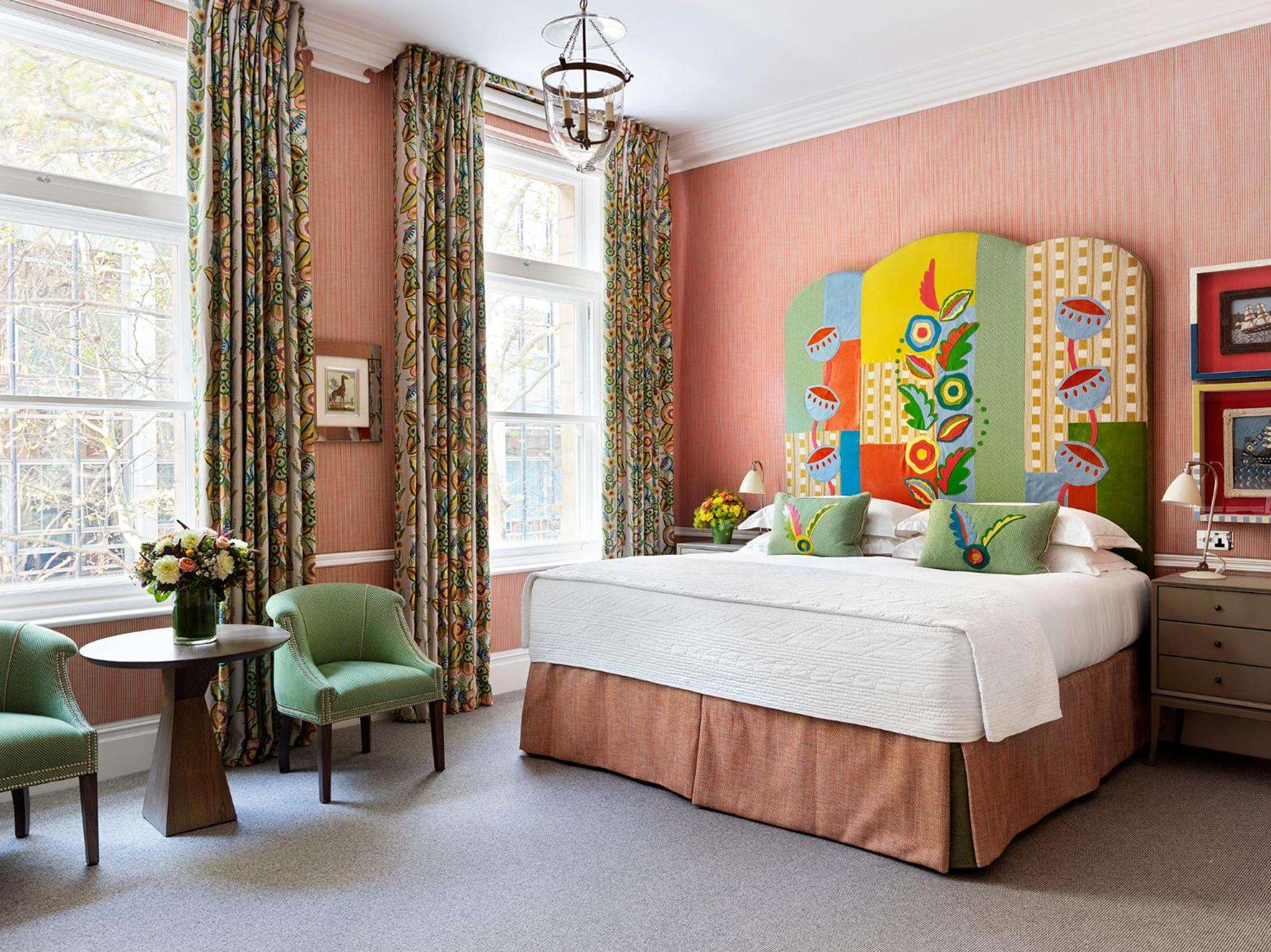 Folk-art florals bloom across a custom headboard while coral grasscloth walls and paisley curtains create an unexpectedly harmonious embrace of pattern and color.