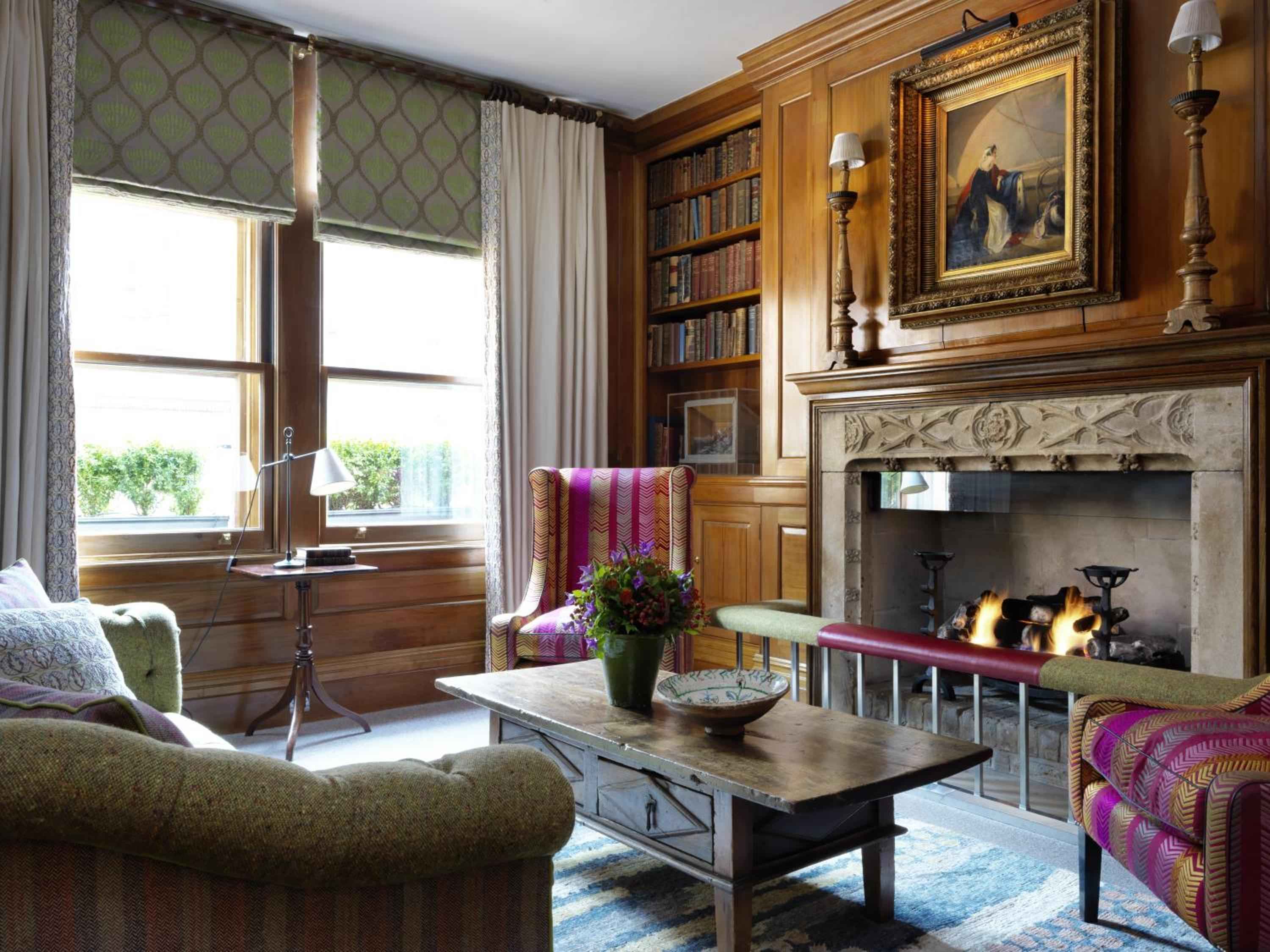 Rich wood paneling and jewel-toned fabrics create an intimate library corner where crackling flames cast dancing shadows across well-worn leather spines and plush seating.