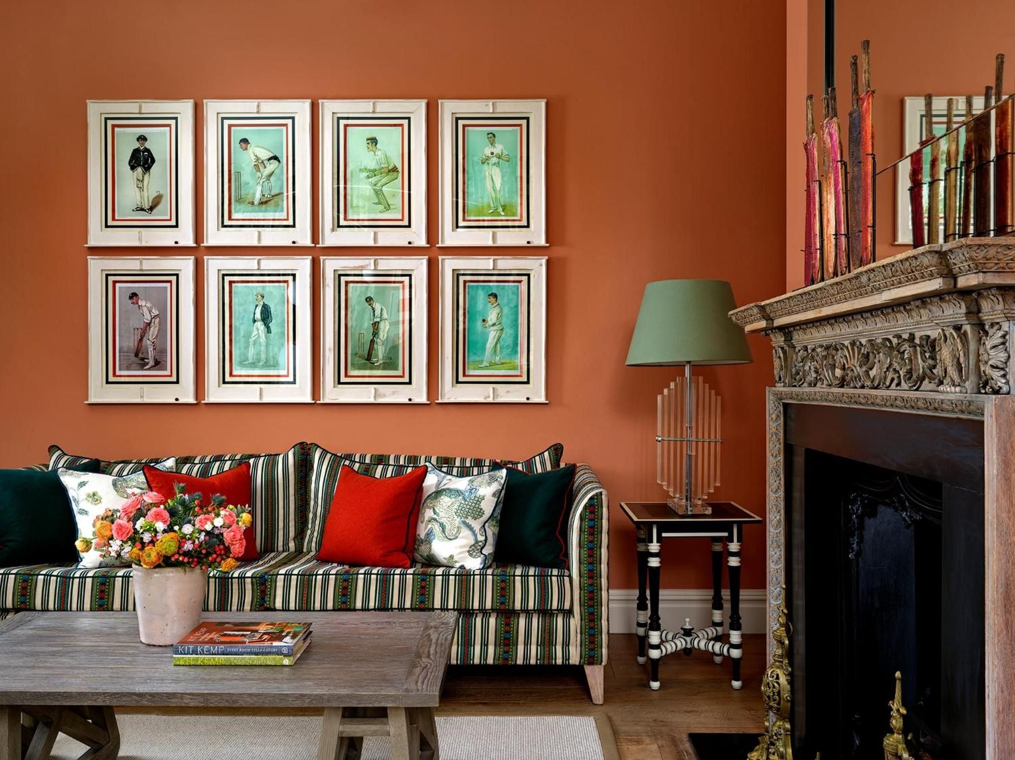 Cricket-themed prints and rich terracotta walls create sporting elegance in this intimate sitting area, where striped upholstery and carved stonework reflect England's heritage.