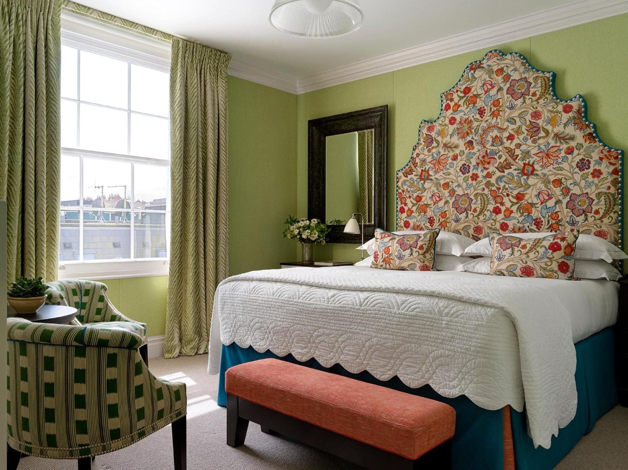 Sage-green walls embrace a bold floral headboard in this charming guest room, where Georgian elegance meets contemporary comfort through layered textures and playful patterns.