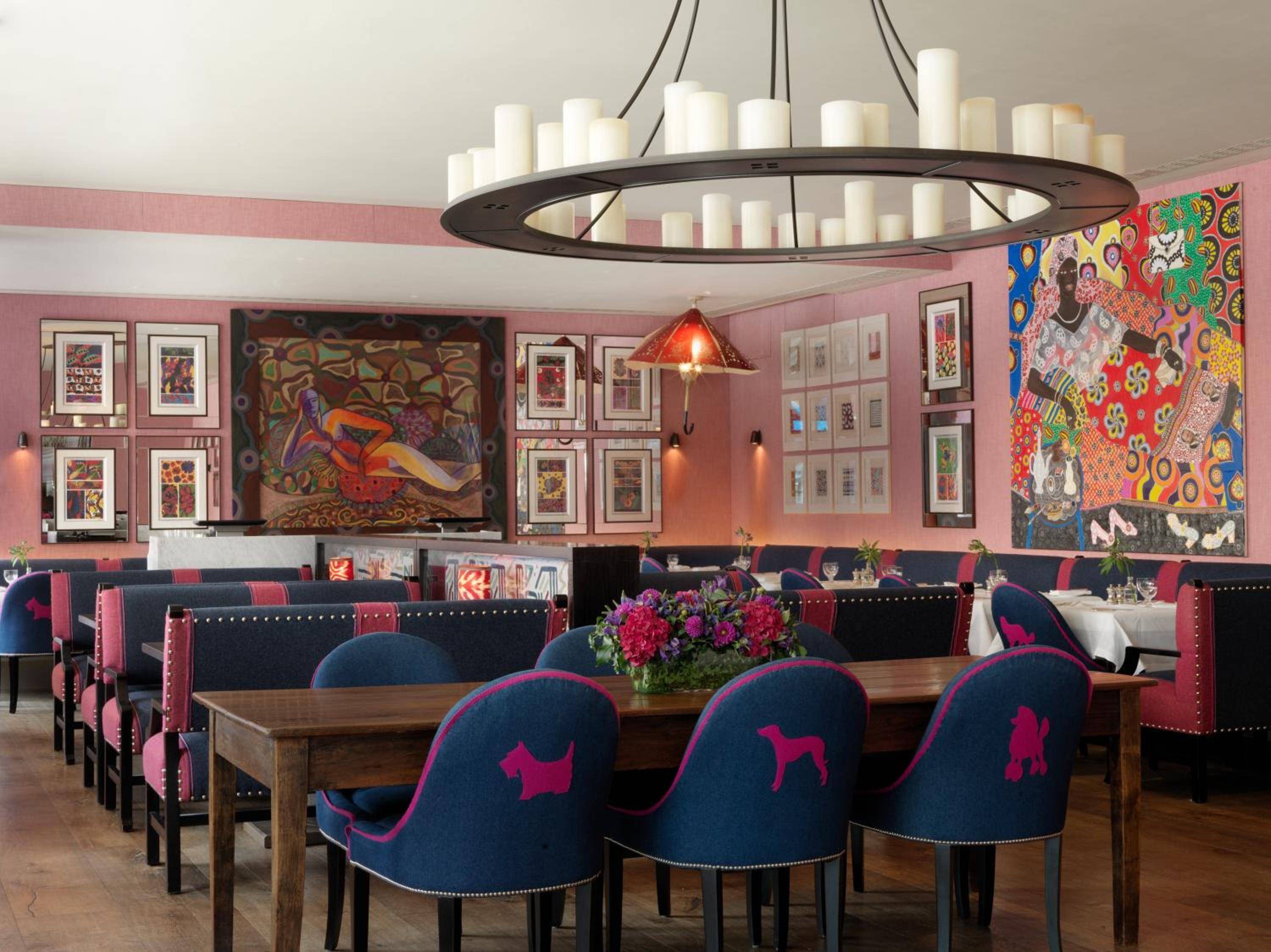 Navy velvet chairs adorned with whimsical dog silhouettes create intimate dining nooks beneath vibrant contemporary art and a striking circular chandelier.