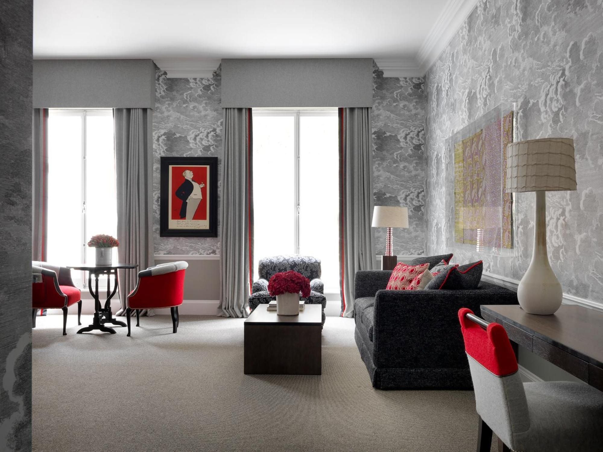Dramatic cloud-patterned wallpaper creates theatrical backdrop for velvet furnishings and crimson accents in this sophisticated living space where modern luxury meets artistic flair.